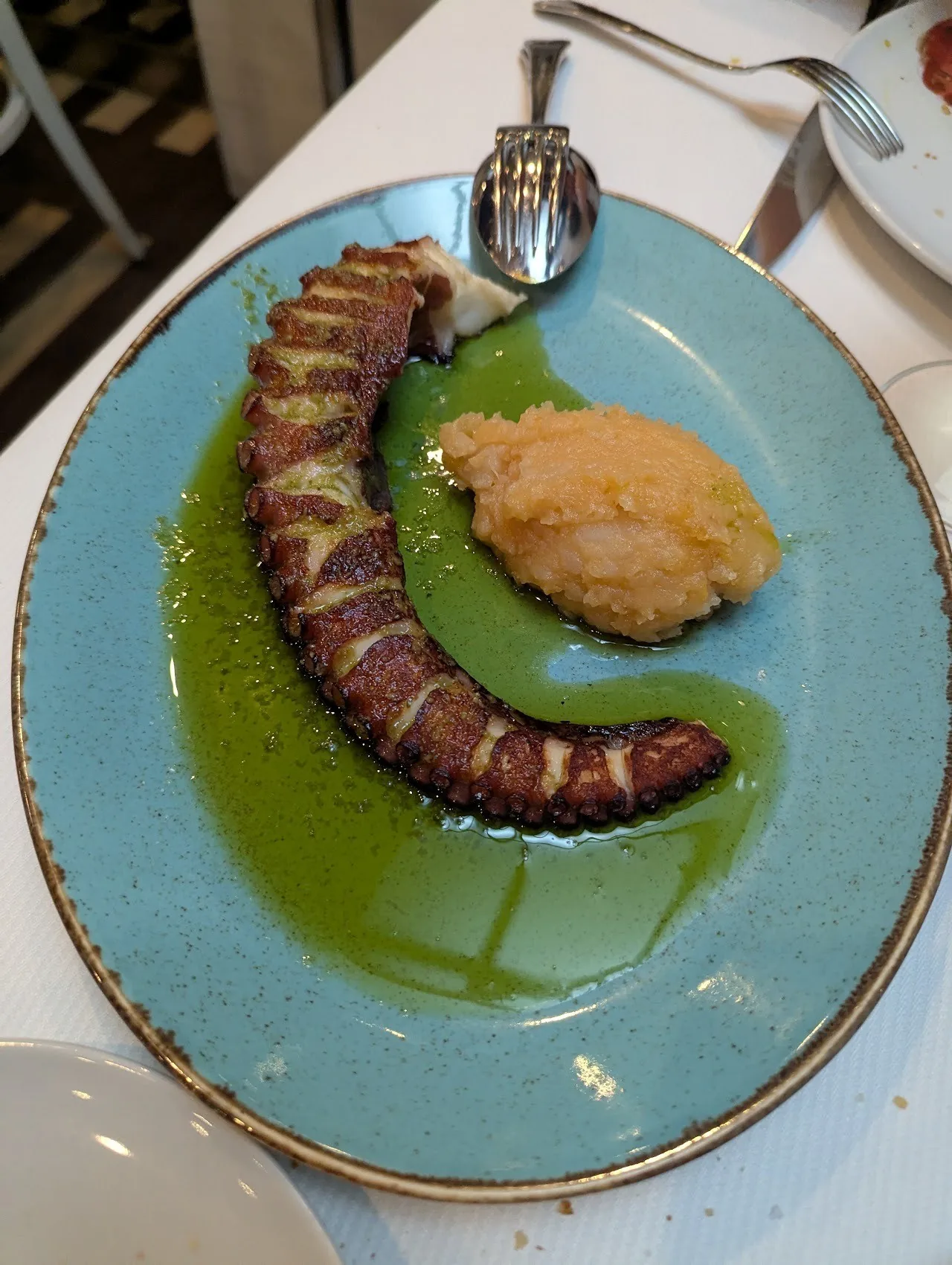 An octopus tentacle with green sauce and a scoop of purée on a blue plate
