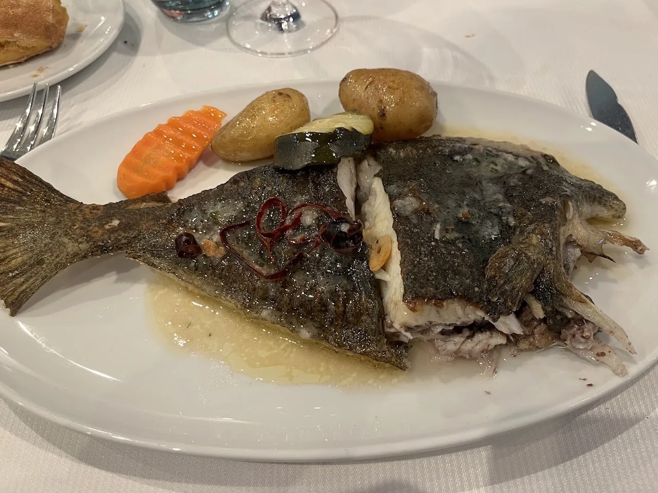 A whole roasted fish with potatoes and carrots on a plate