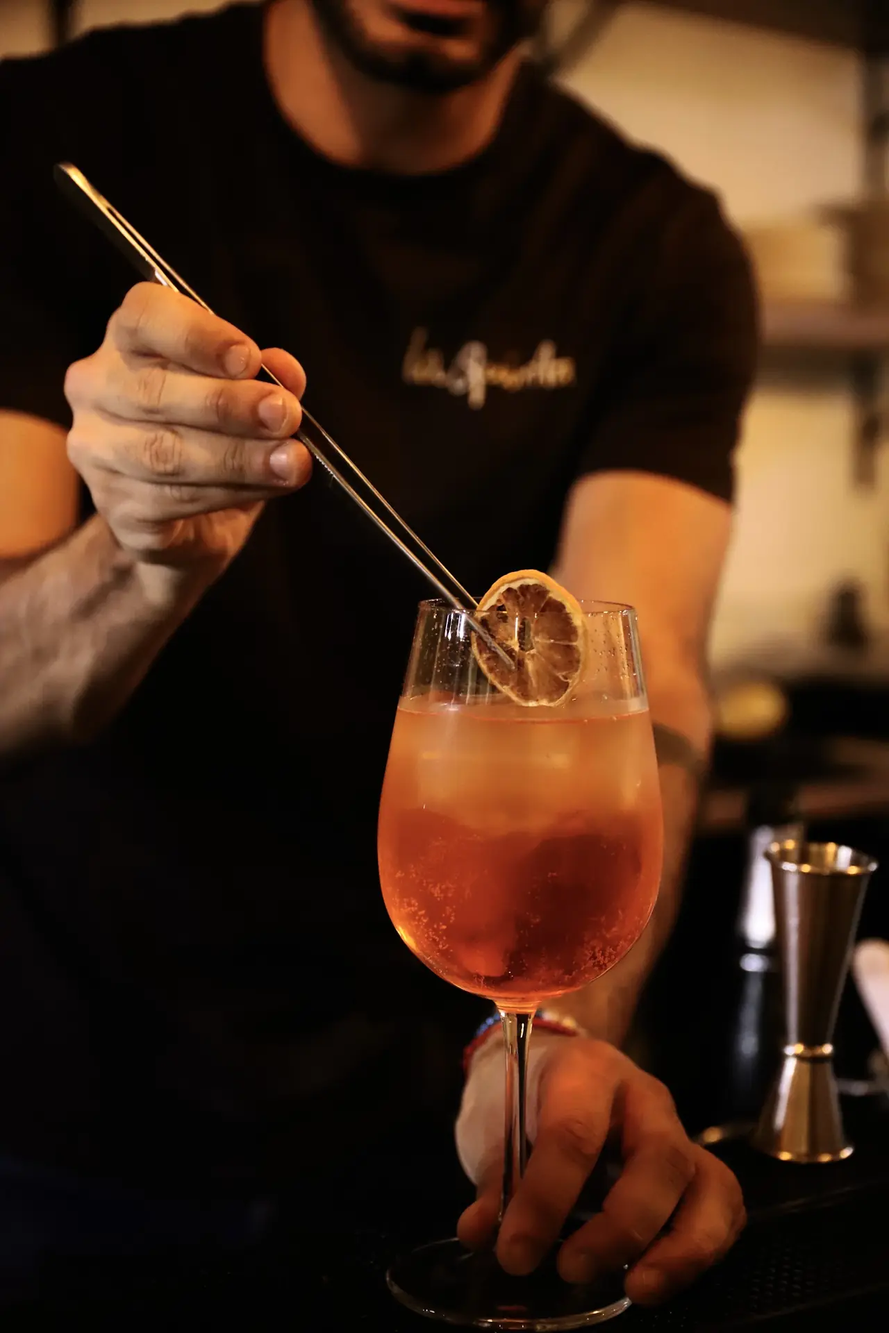 Bartender using tweezers to place a dried orange slice on an orange spritz cocktail in a wine glass