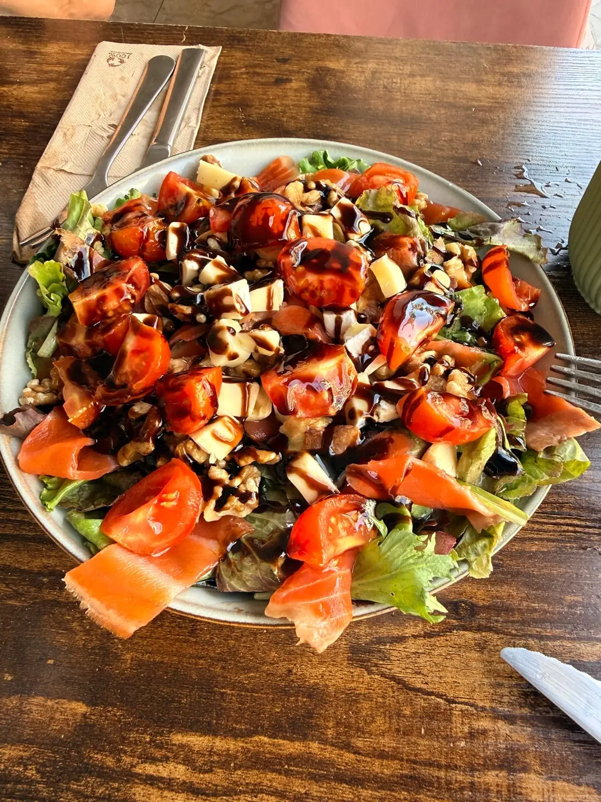 Salad with cherry tomatoes, smoked salmon, walnuts, cheese cubes and balsamic drizzle over lettuce