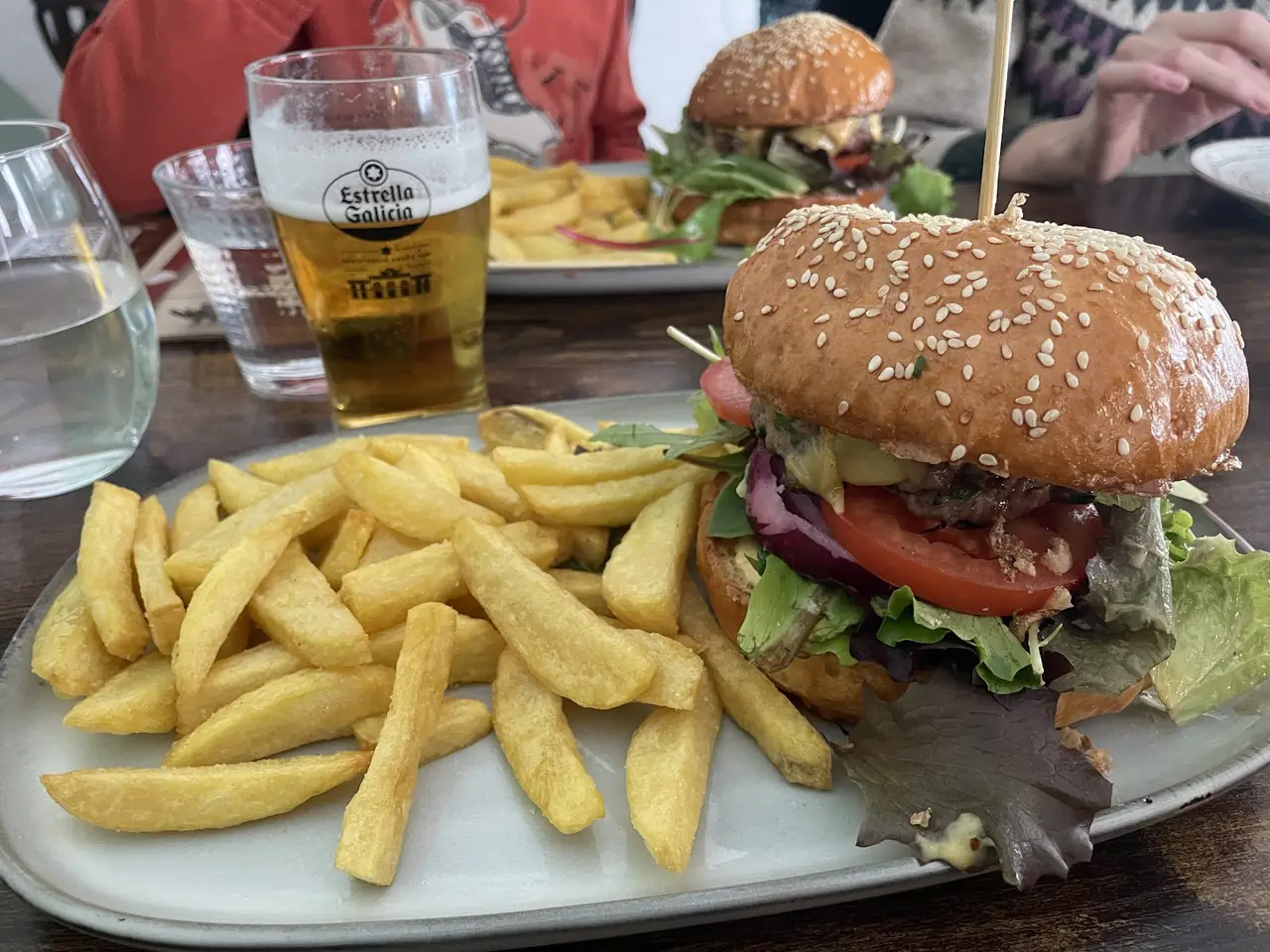 Sesame-bun burger with tomato, red onion and lettuce beside a plate of fries and a glass of beer