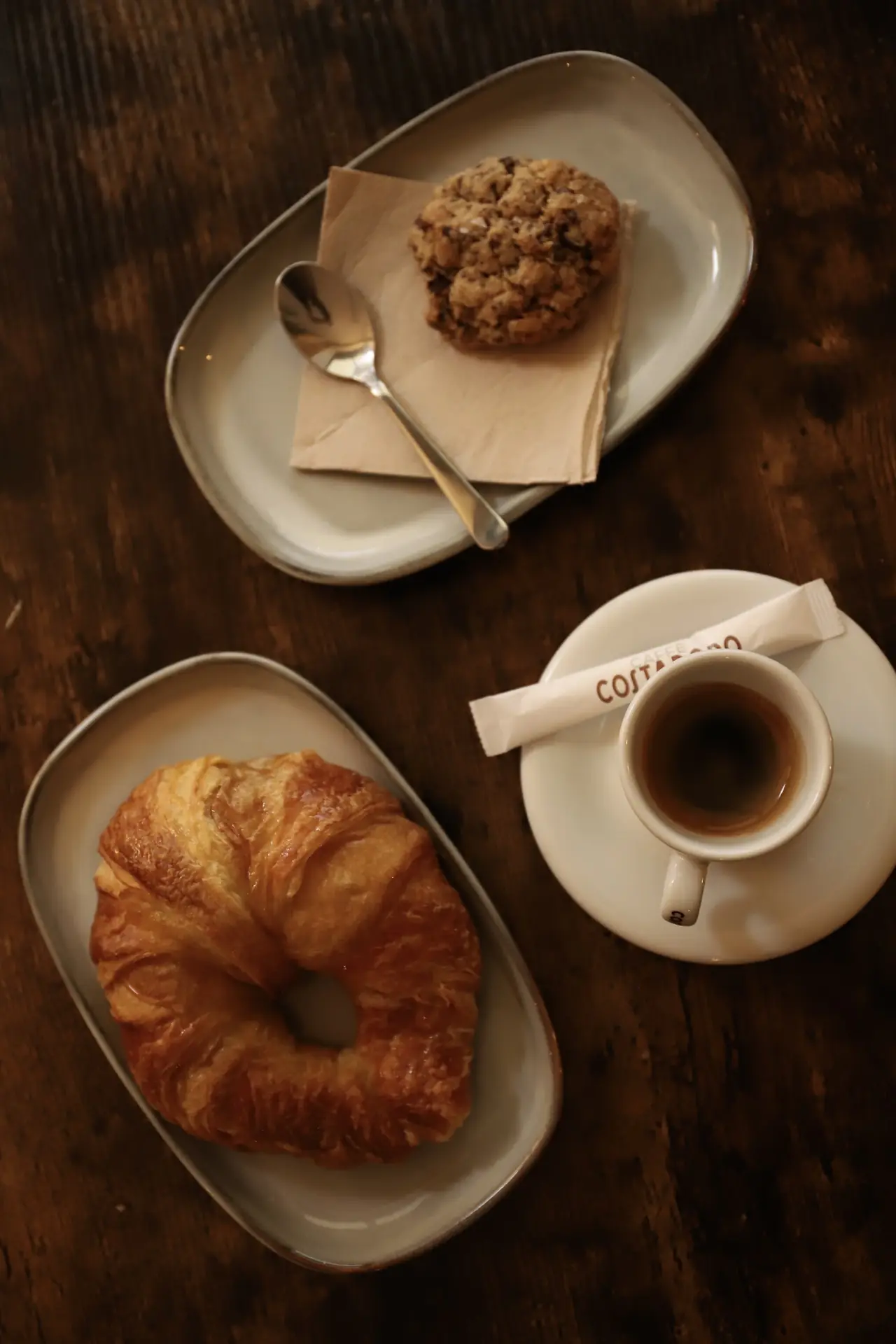 Butter croissant, a chocolate chip cookie and an espresso served on separate plates