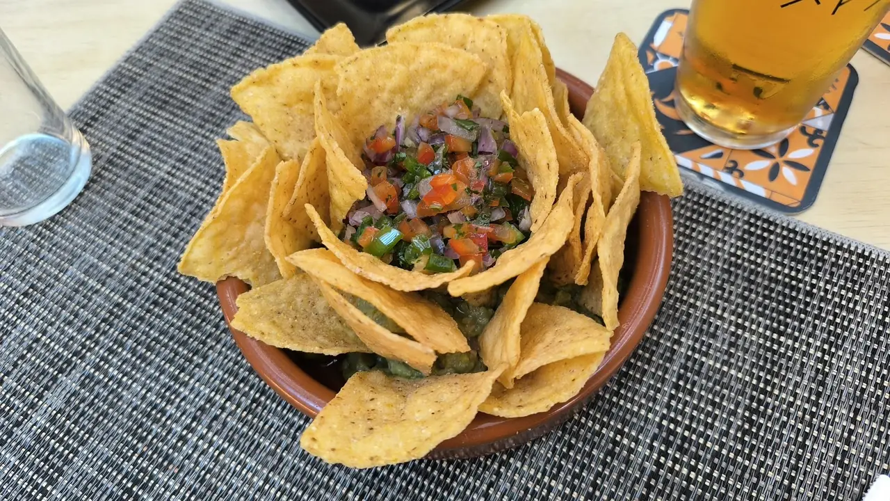Bowl of tortilla chips with pico de gallo and guacamole beside a glass of beer