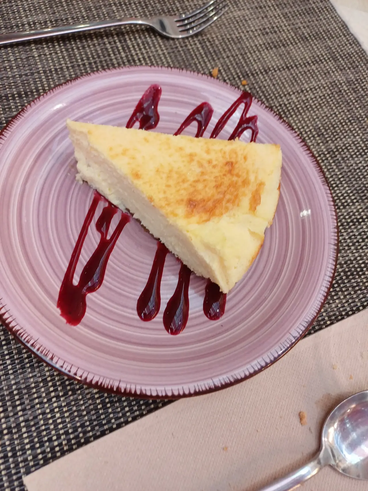 Slice of baked cheesecake with red berry sauce drizzle on a pink plate