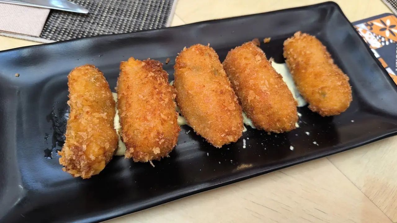 Five fried croquettes on a black rectangular plate with a sauce drizzle