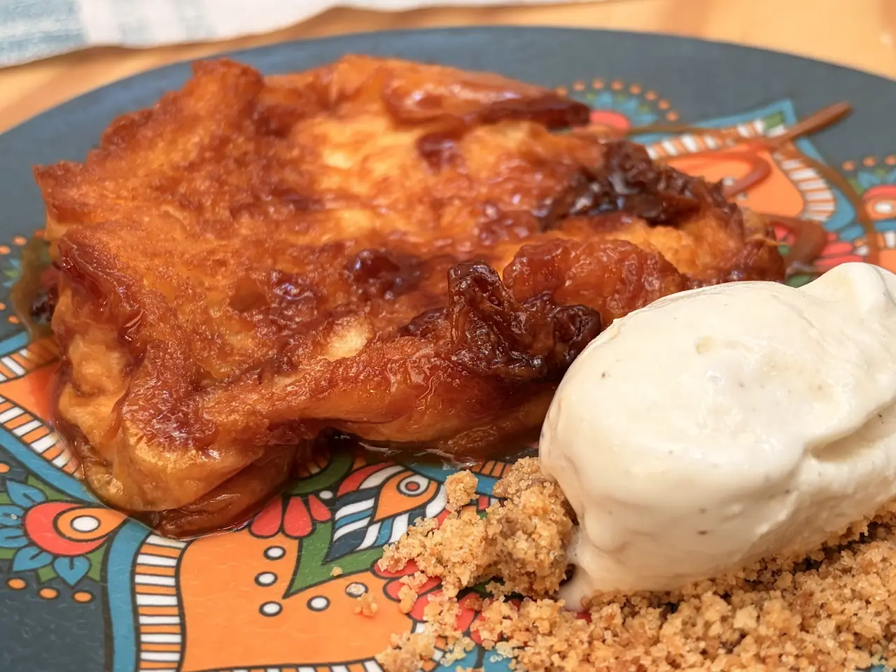 Caramelized bread pudding dessert with a scoop of ice cream and crumble on a patterned plate