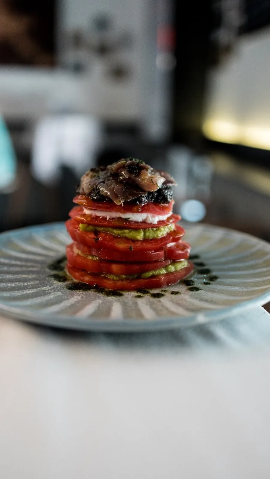 A stacked tomato tapa topped with dark slices on a blue patterned plate