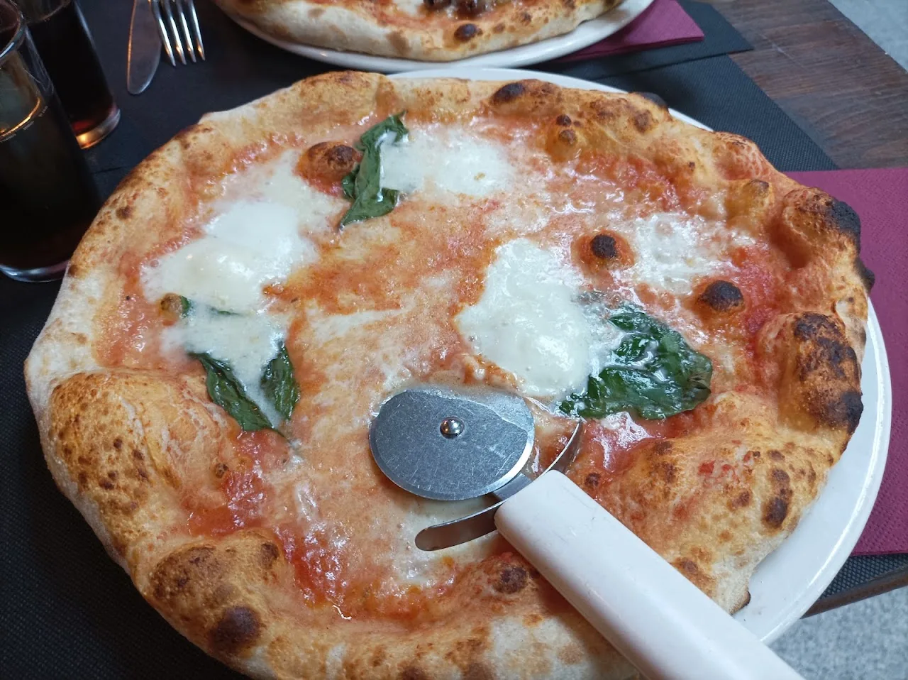 A margherita pizza with basil being sliced with a rolling cutter