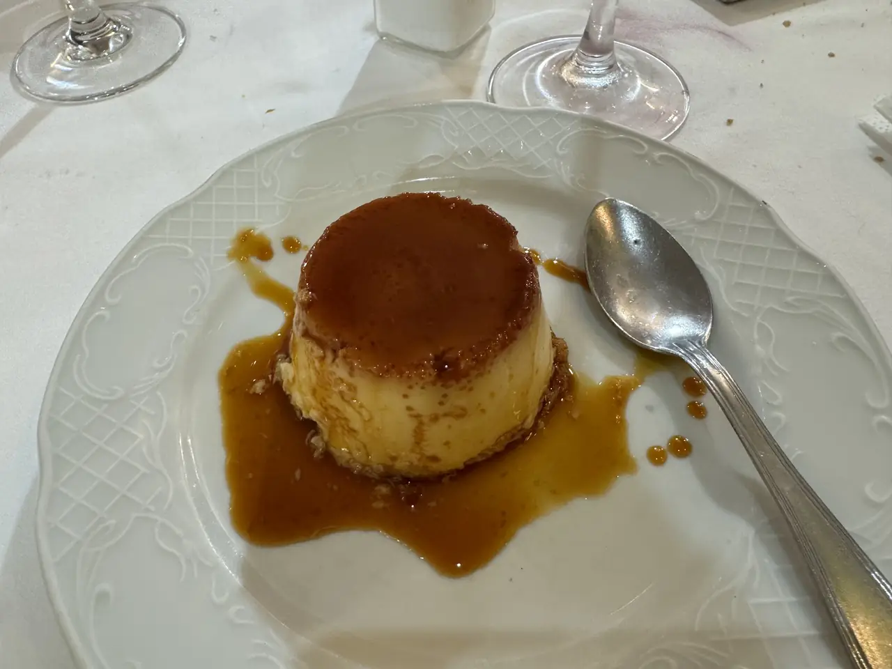 A caramel flan on a white plate with a spoon