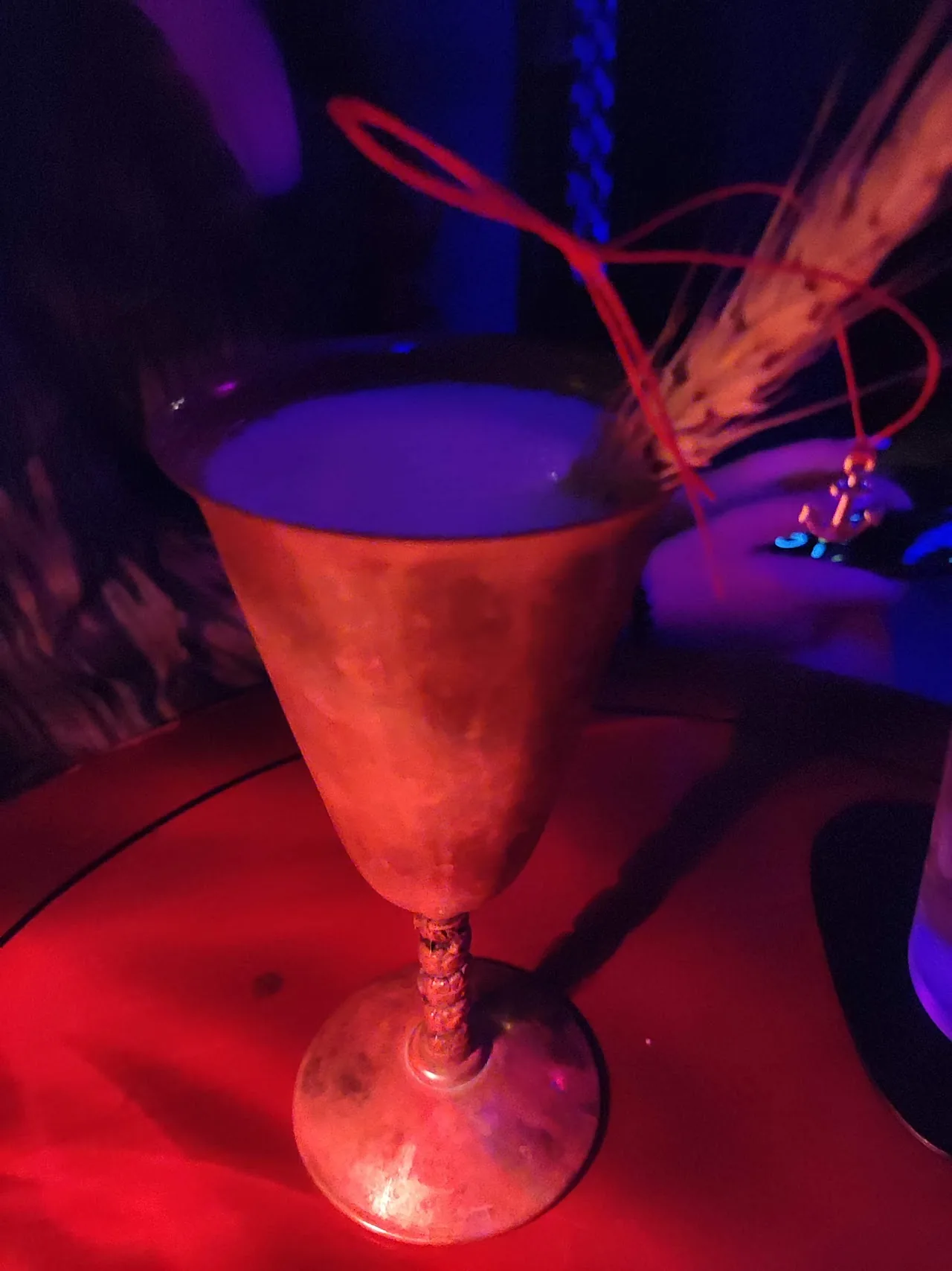 A martini-style cocktail with garnish in a stemmed glass under red and blue light