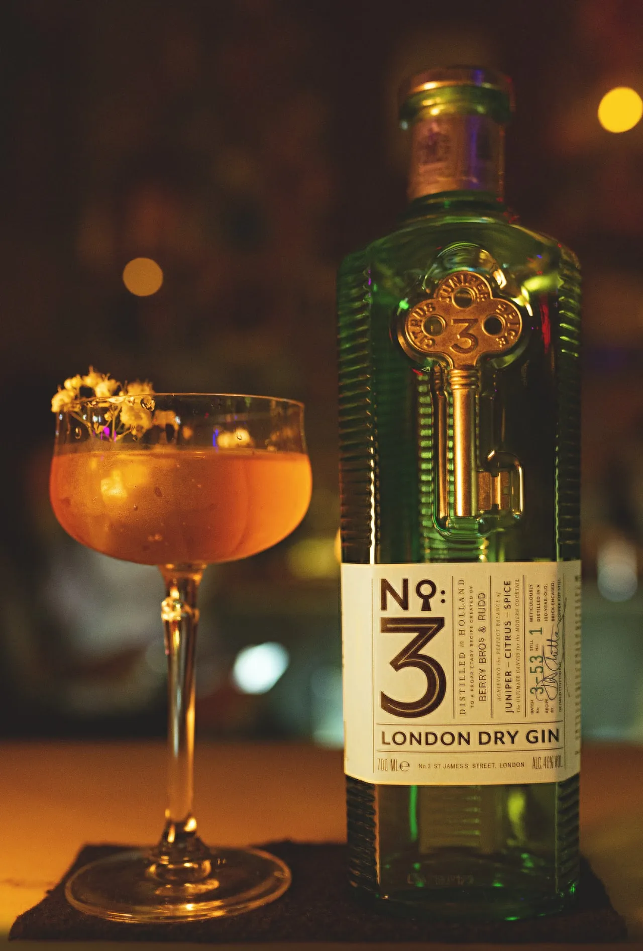 An orange cocktail with a flower garnish next to a gin bottle