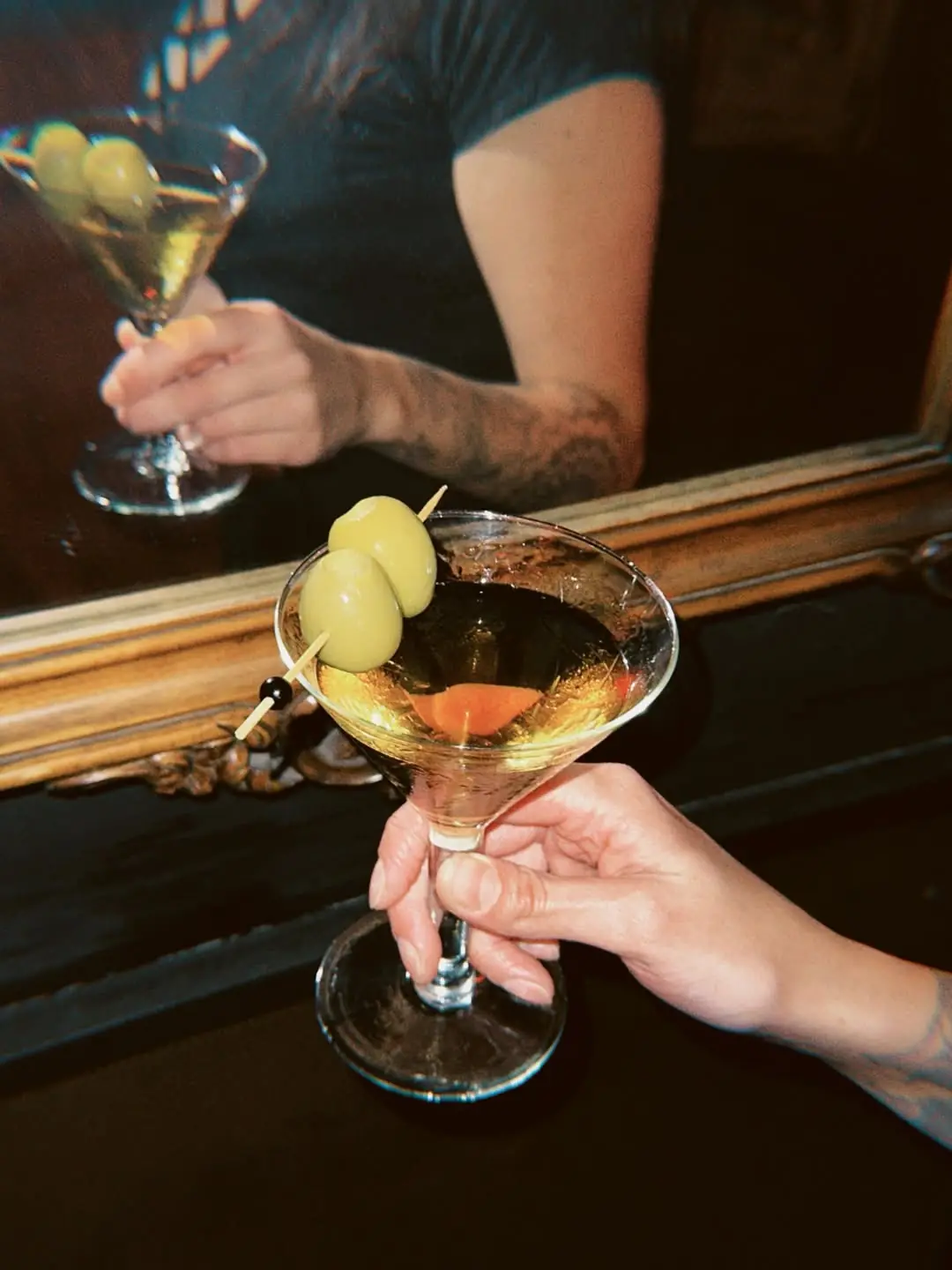 Two martini glasses with olive garnishes being held up together