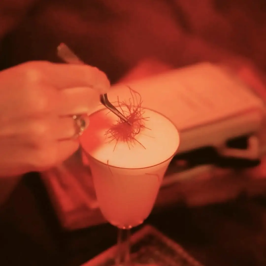Hand garnishing a pale pink cocktail with a dried flower