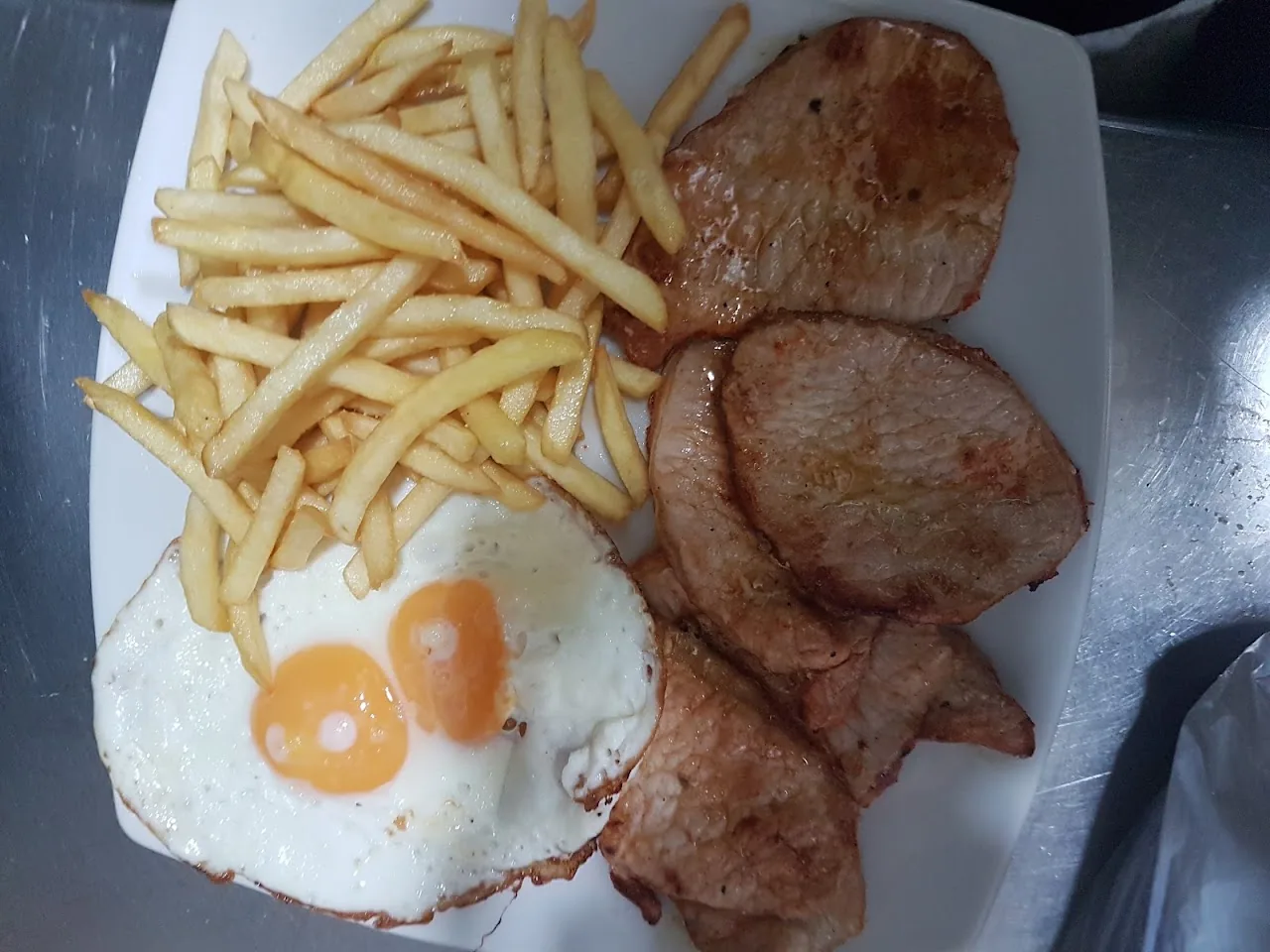 A plate of fried eggs with fries and bacon