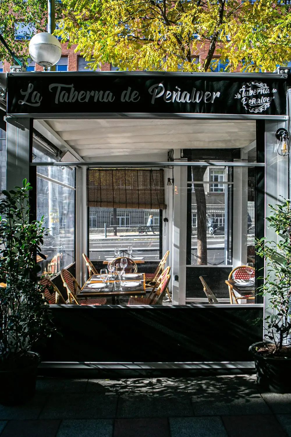 Glass-fronted terrace entrance of La Taberna de Penalver with set tables and rattan chairs, awning sign above