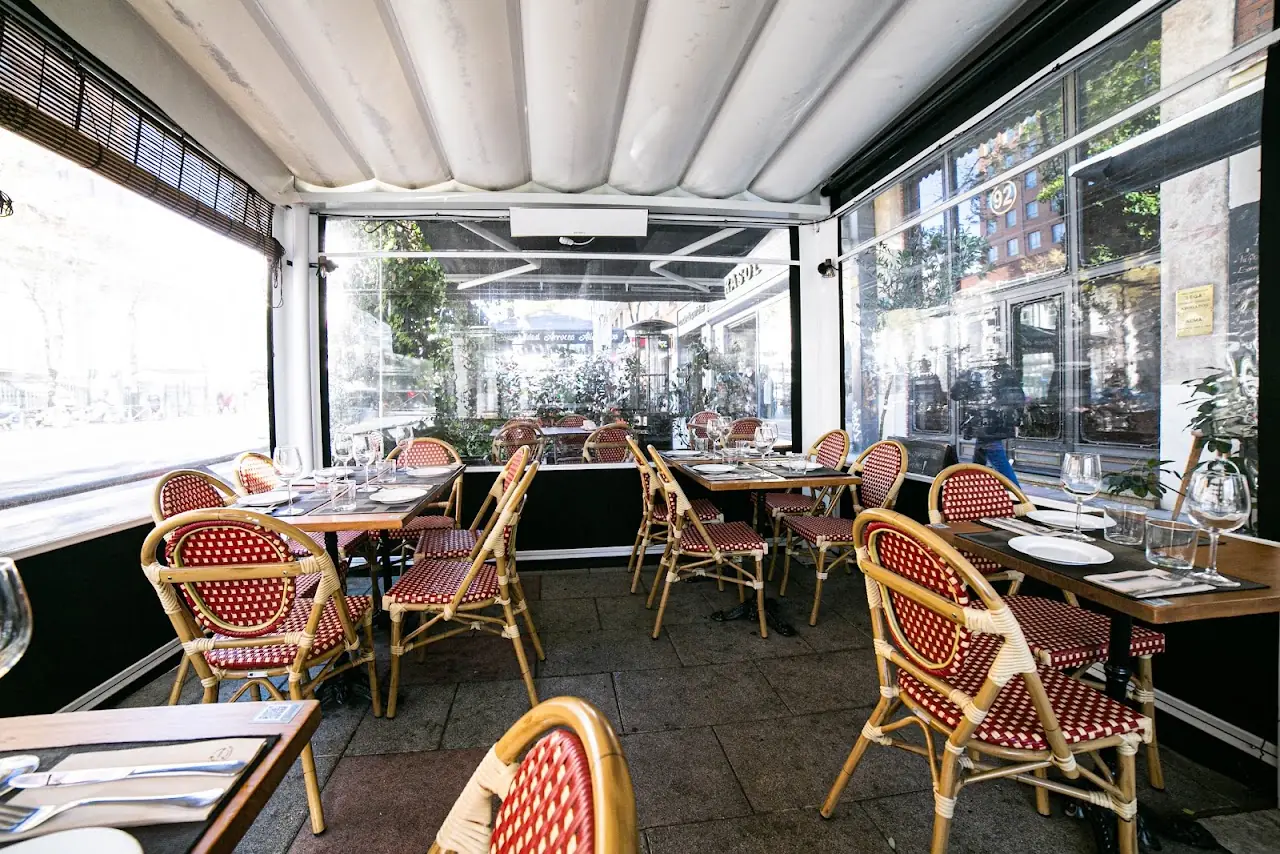 An empty covered terrace with wicker bistro chairs and set tables.