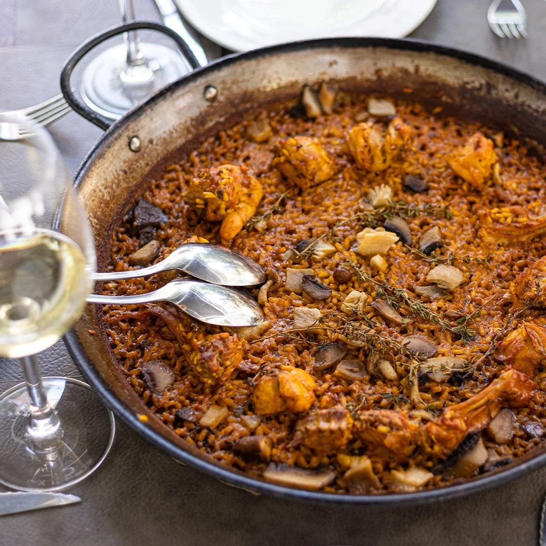 A paella with meat and vegetables on the table with wine