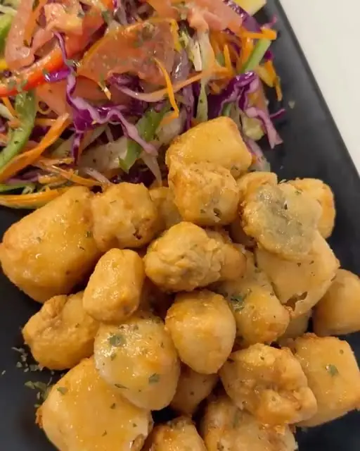 Golden fried battered pieces with chopped herbs beside a shredded cabbage, carrot and tomato salad on a black plate