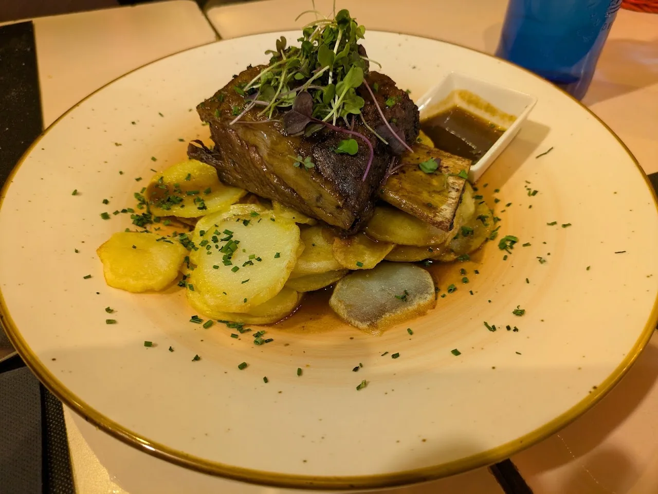 A seared meat dish with baby potatoes and a small sauce cup