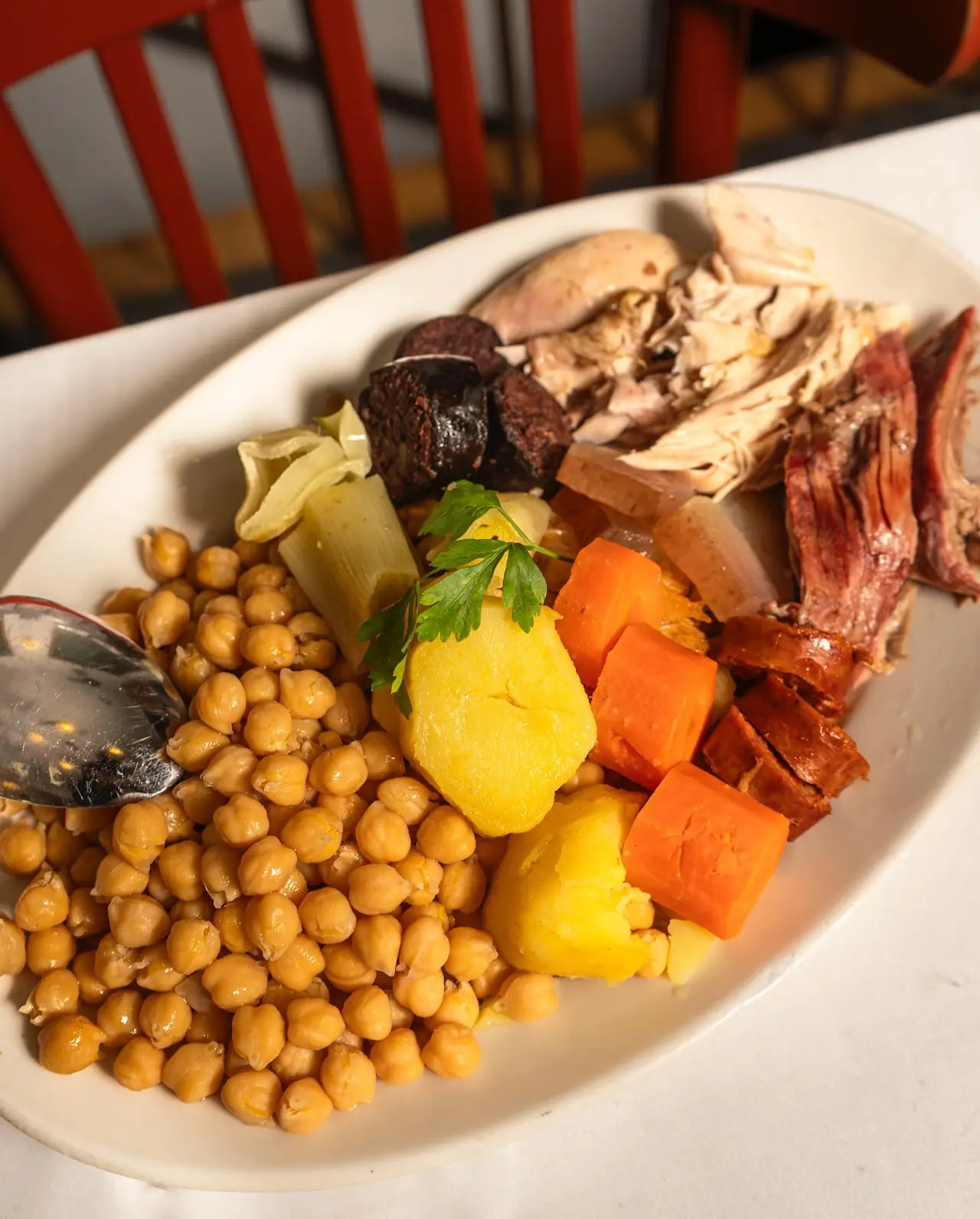 Oval plate of cocido madrileno with chickpeas, boiled potato, carrot, leek, morcilla, chorizo, chicken and rib meat