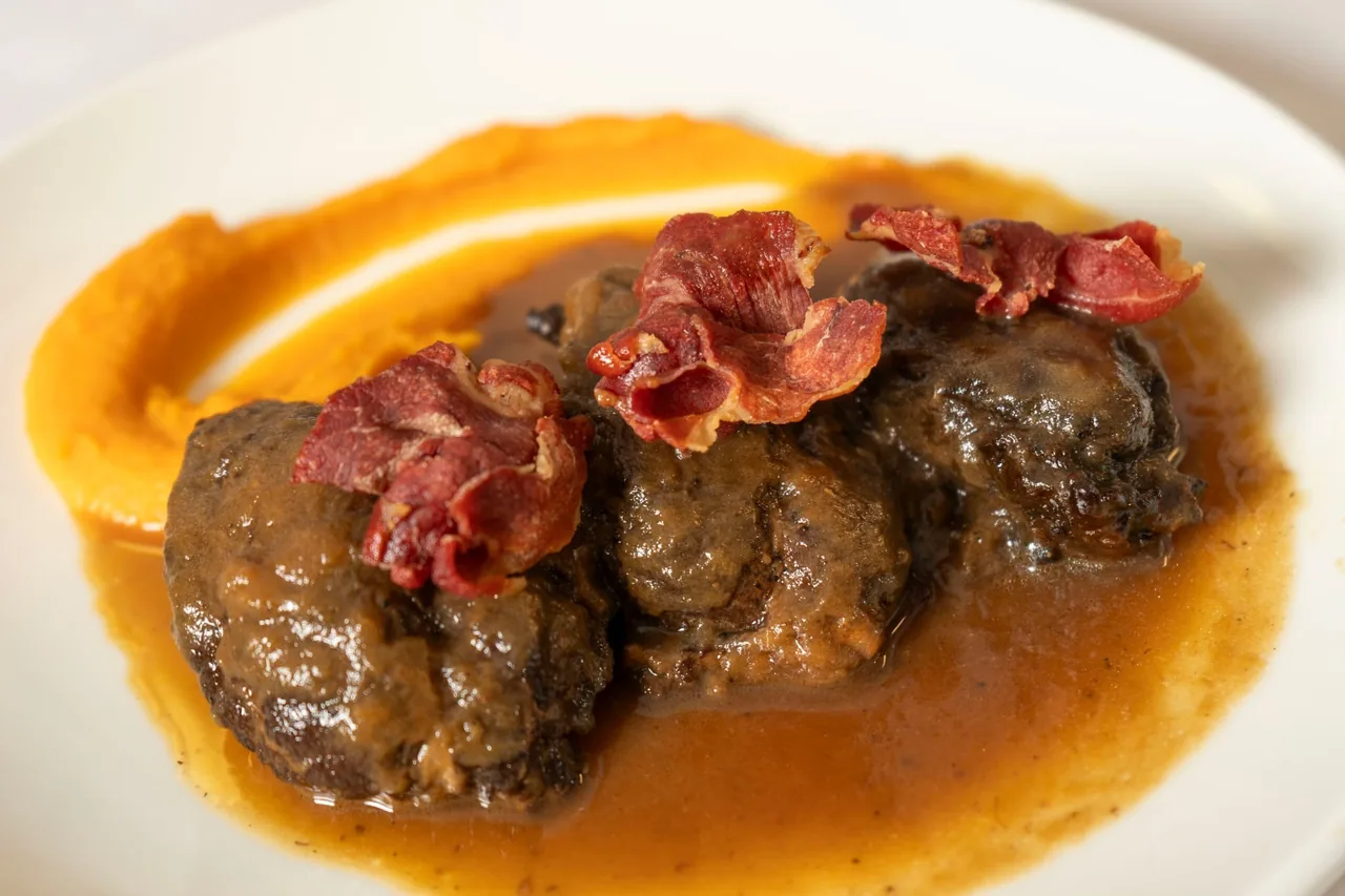 Braised meat in a rich sauce with slices of cured ham on a white plate