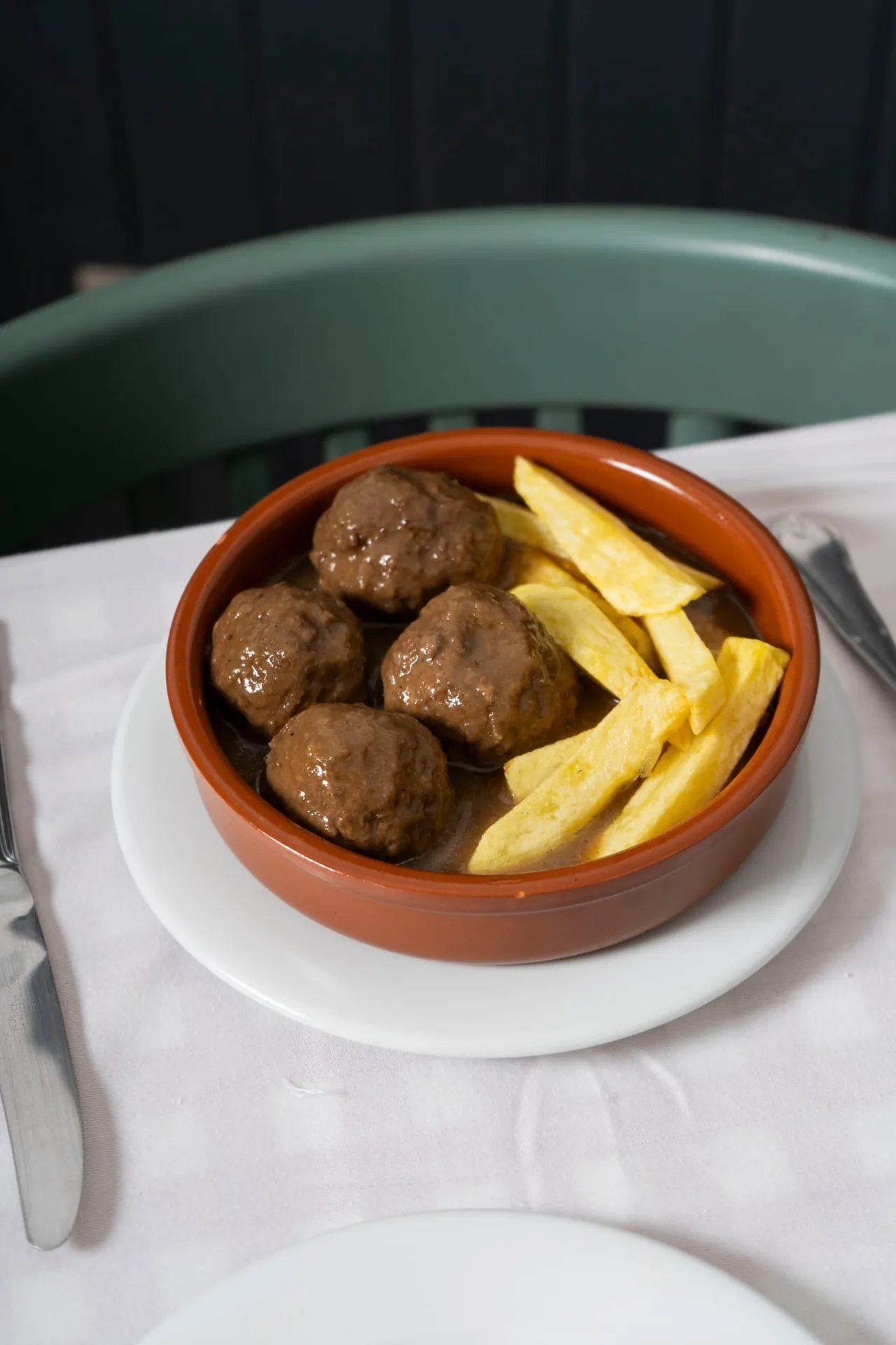 A terracotta dish of meatballs with fries on a white plate