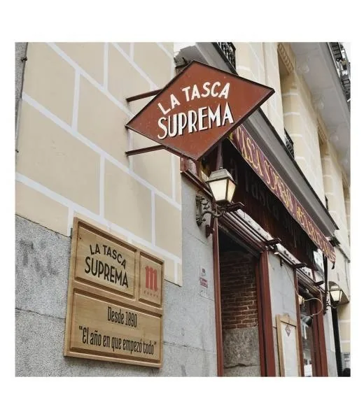 A diamond-shaped hanging sign and a wooden plaque with lettering on a building wall.