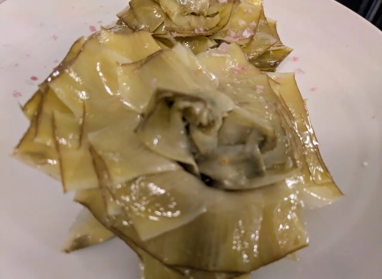 Whole braised artichoke opened on a plate, leaves glossy with olive oil