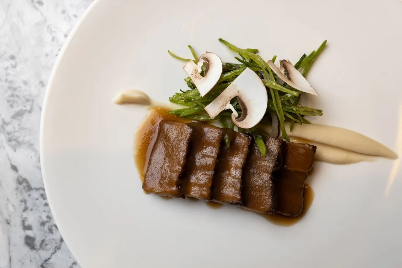 Slices of dark cooked meat with mushrooms and salad leaves on a white plate