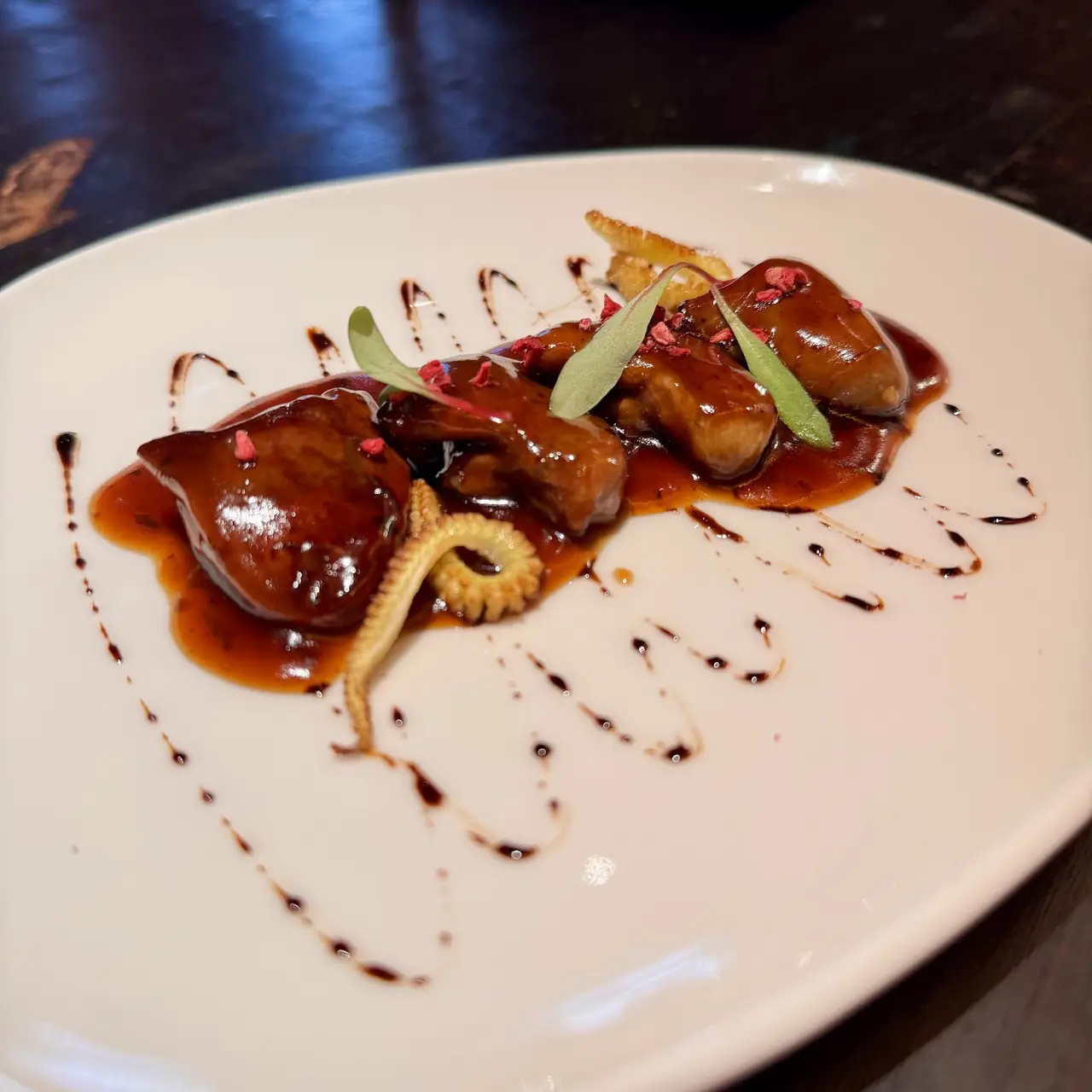 Braised meat pieces in glossy dark sauce with balsamic drizzle and herb garnish