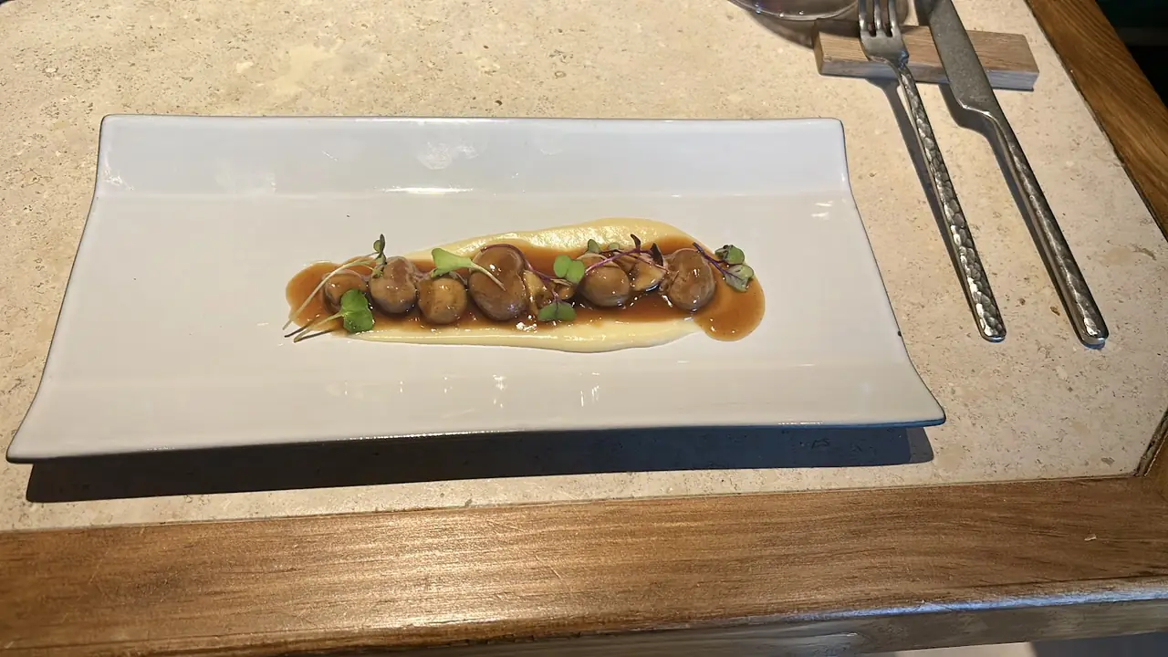 Row of small braised bites on cream puree with jus and microgreens on rectangular plate