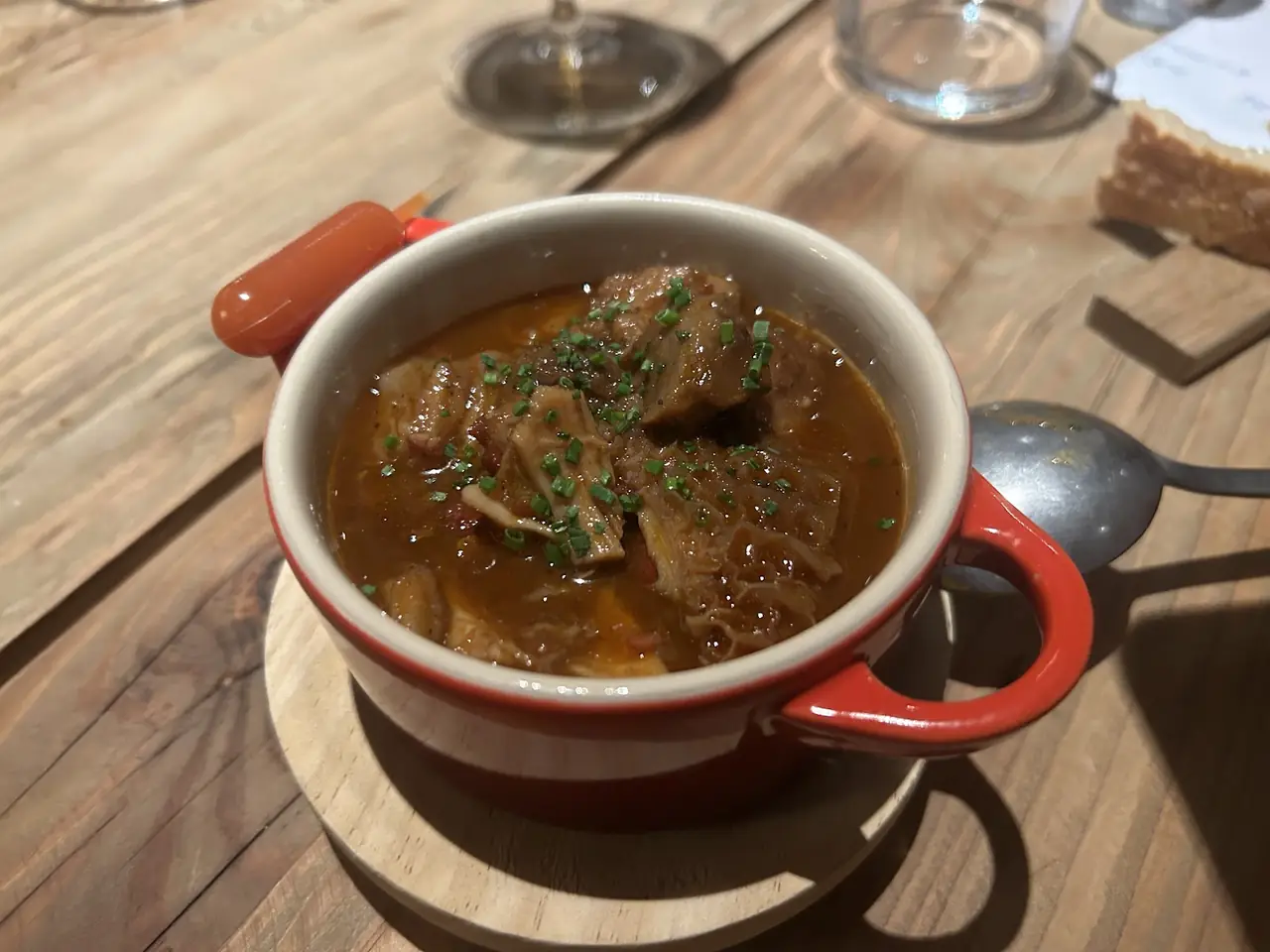 Stew with meat pieces and chives in a red-and-white ceramic bowl on a wooden table
