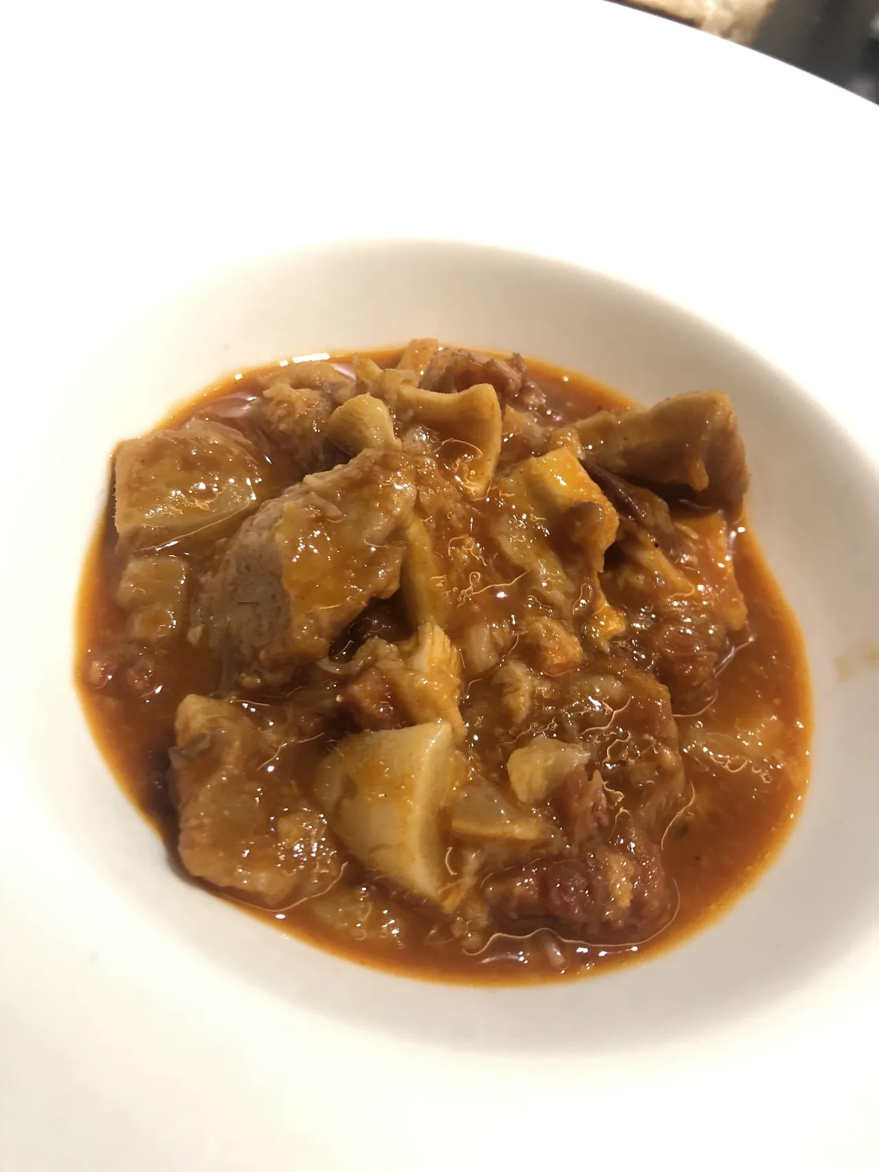 A white bowl of tripe stew in a thick red-brown sauce