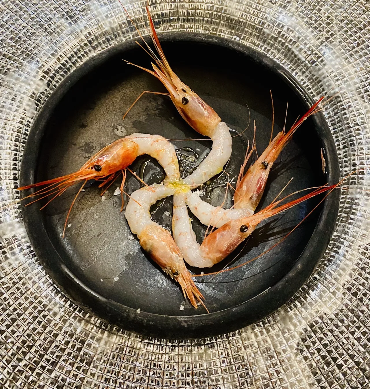 Several red prawns arranged in a swirl on a dark round plate