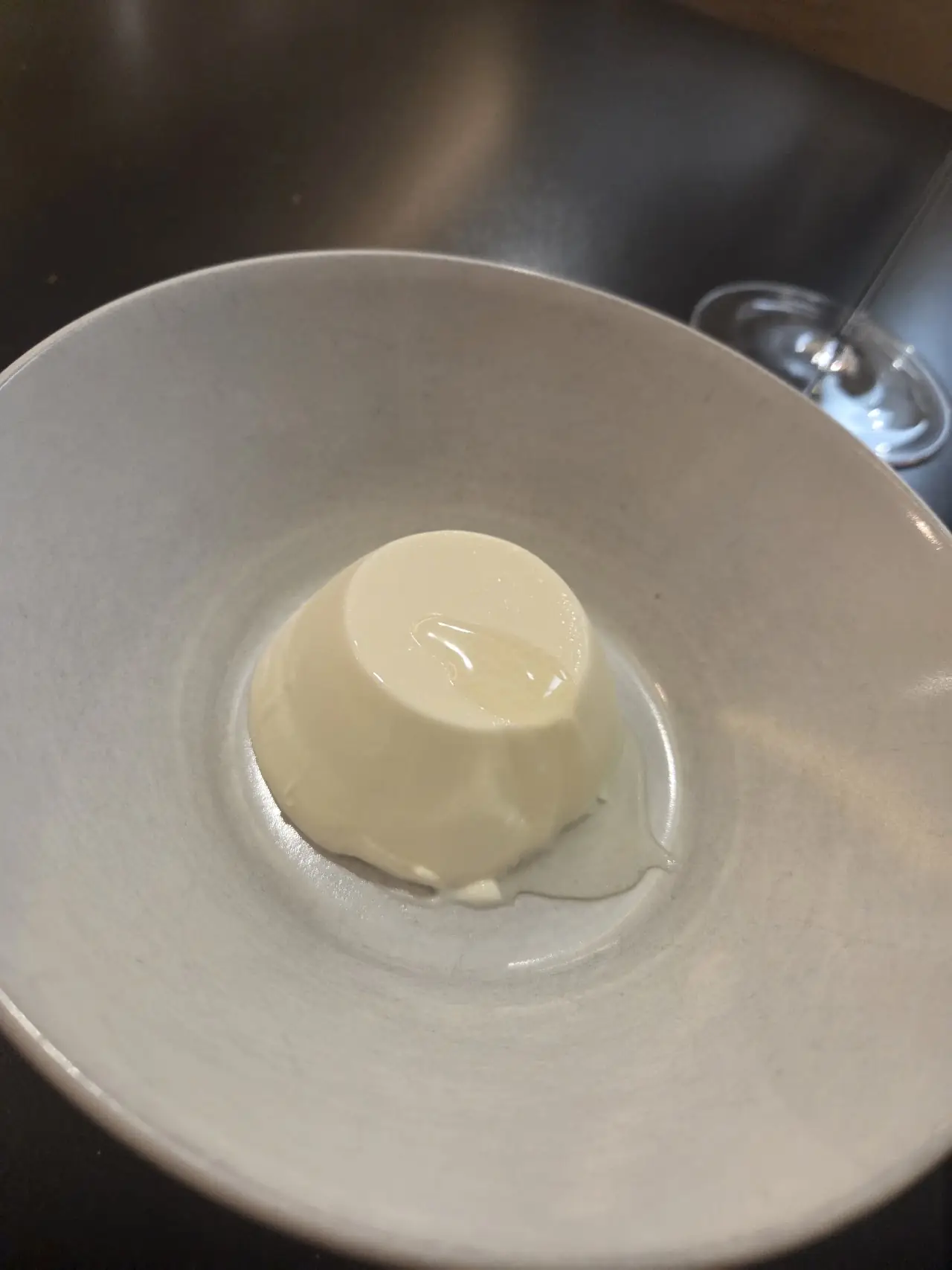 A small dome of pale set cream in a shallow white bowl with a pooled sauce