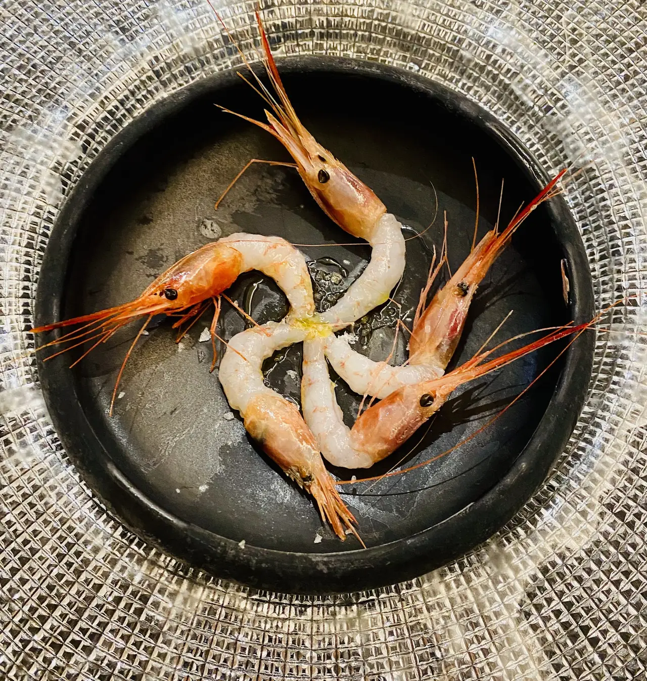 Raw whole prawns arranged in a circle in a dark bowl with olive oil and salt