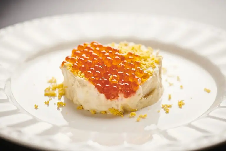 Plated dish of creamy base topped with orange roe and crumbled egg yolk on a white plate