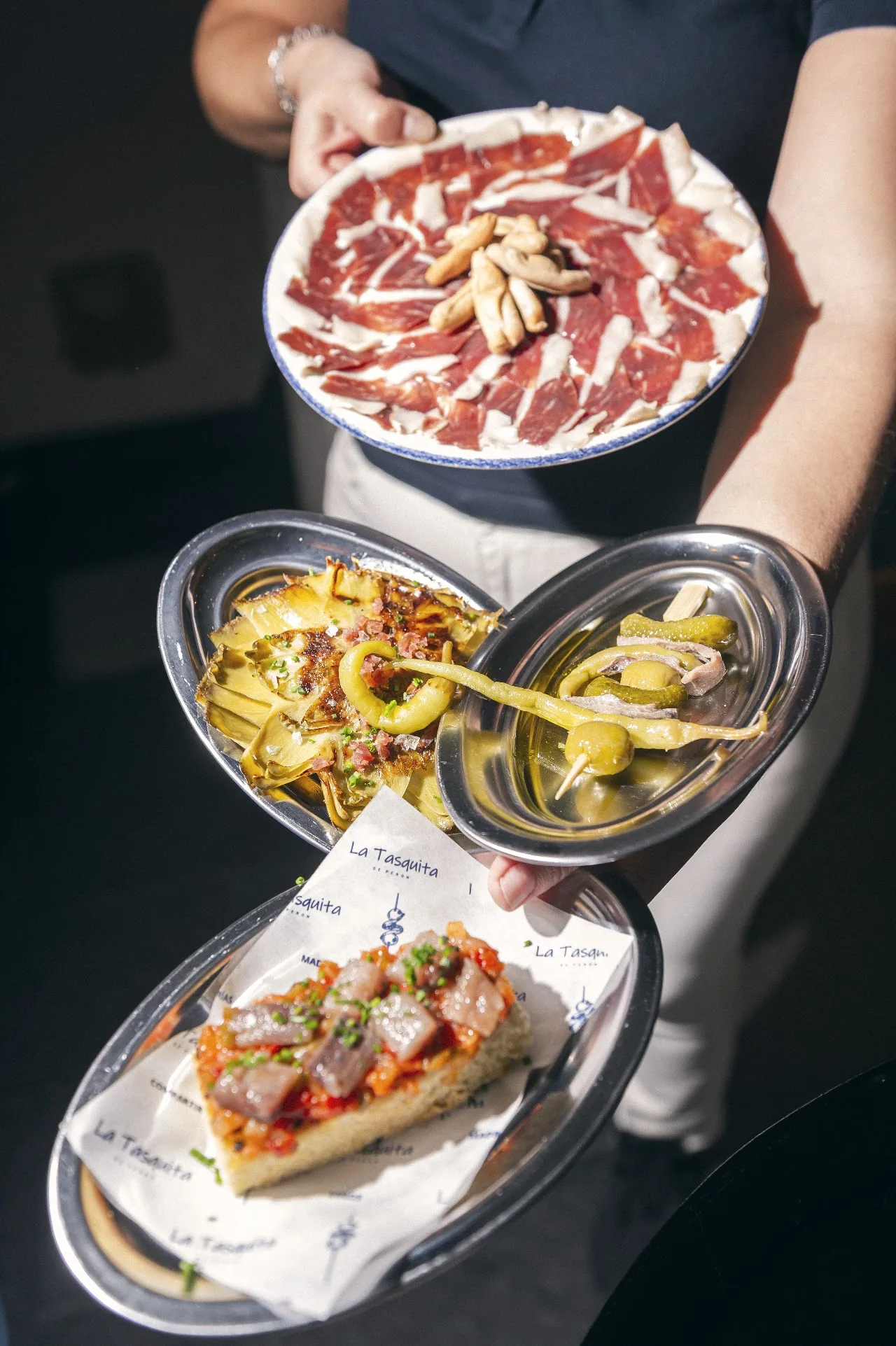 A server holding plates of jamón, croquetas and a savory tart