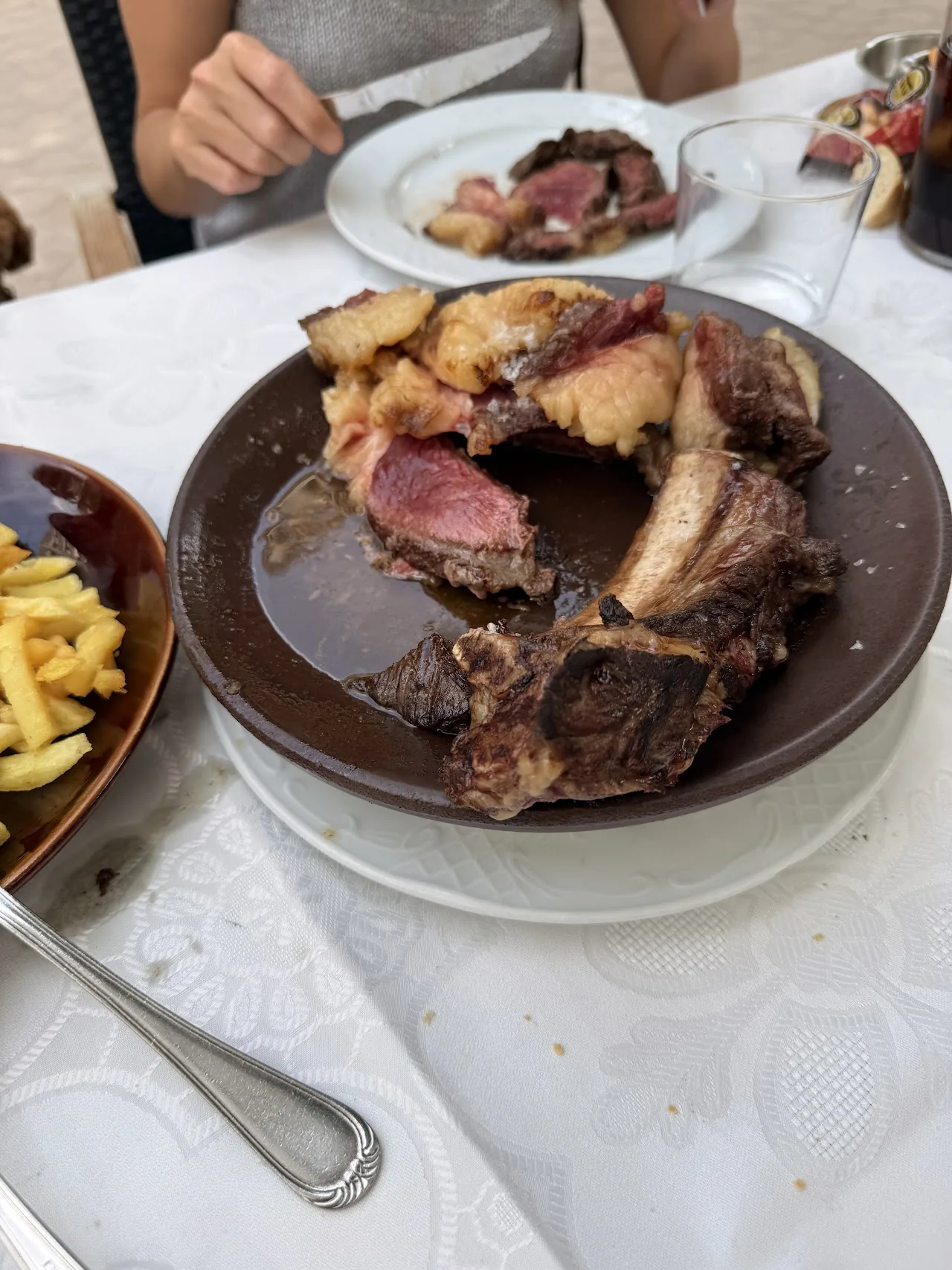 A diner's hand cutting into a plate of grilled ribs in sauce