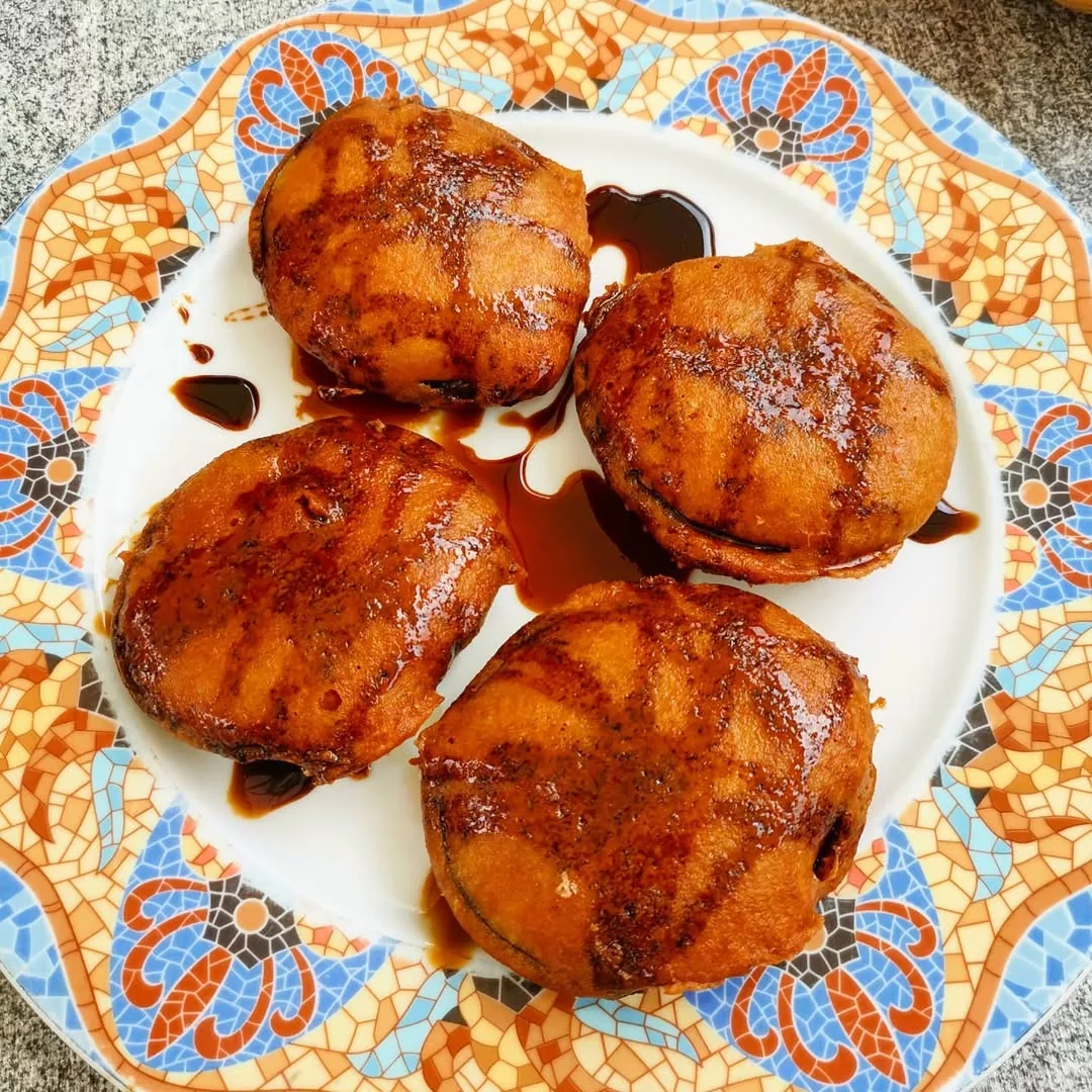Four glazed meat pieces in dark sauce arranged on a decorative floral-patterned plate