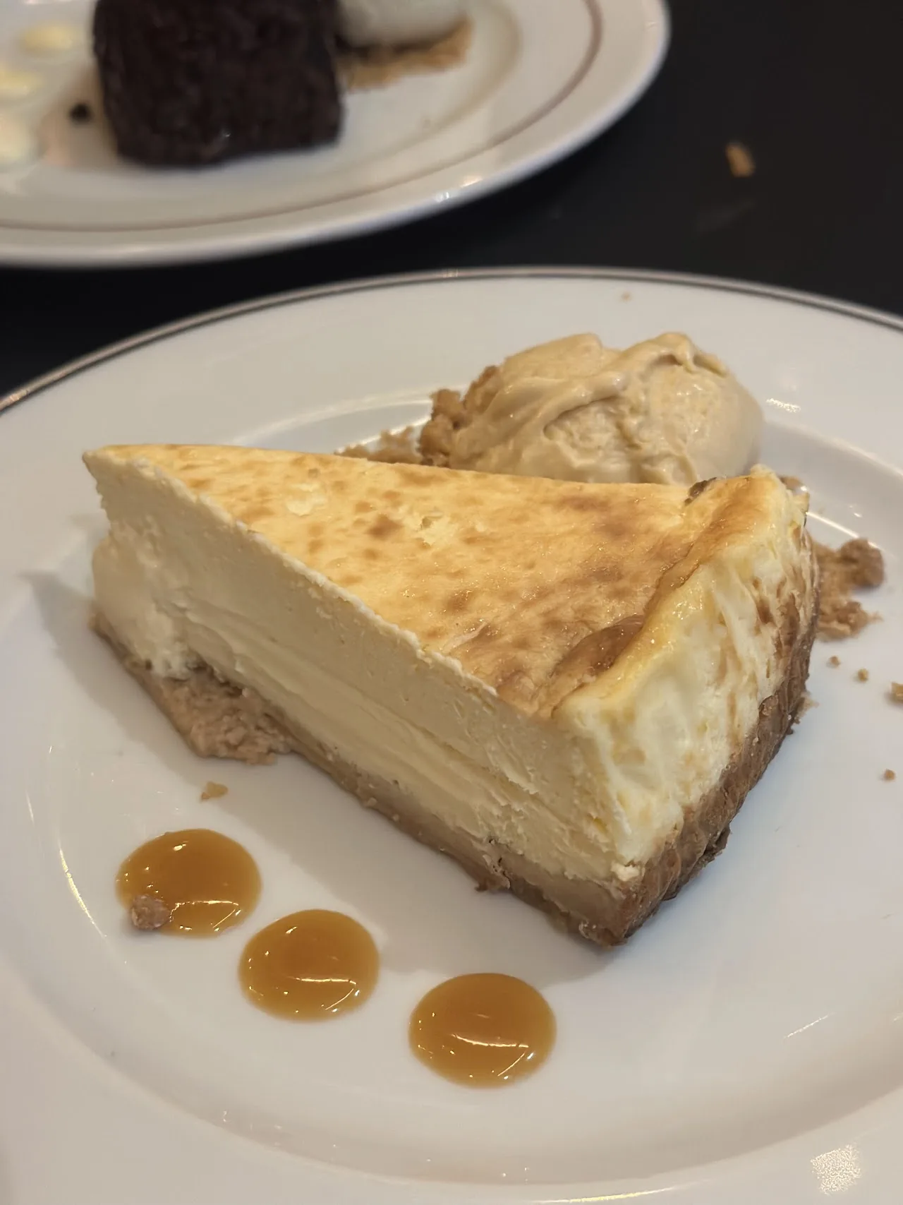 A slice of cheesecake with caramel drizzle and a scoop of ice cream