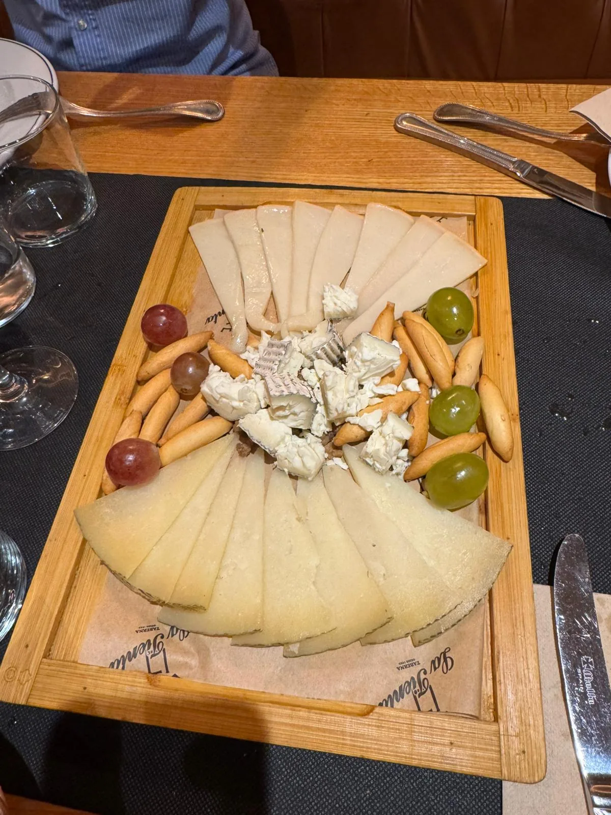A wooden cheese board with assorted cheeses, olives and nuts