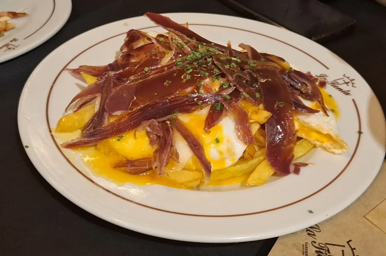 A plate of fried egg over potatoes topped with cured ham slices