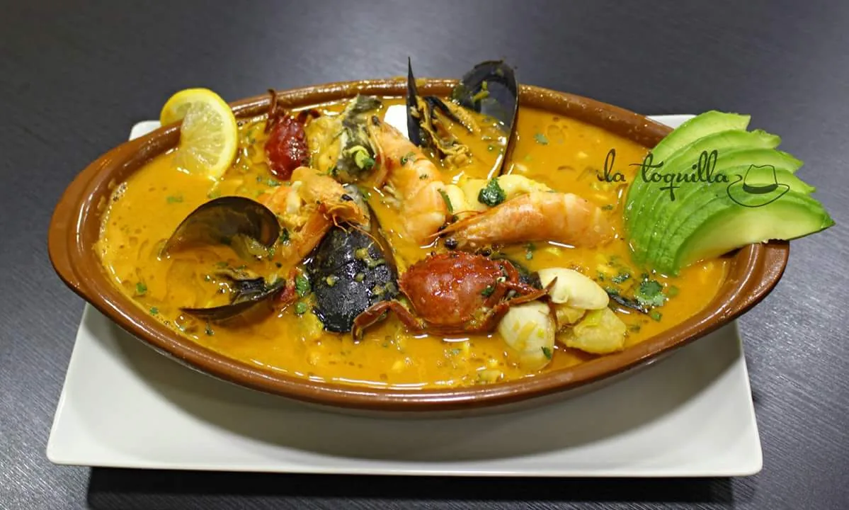 A seafood stew with mussels, shrimp, and avocado in a clay dish