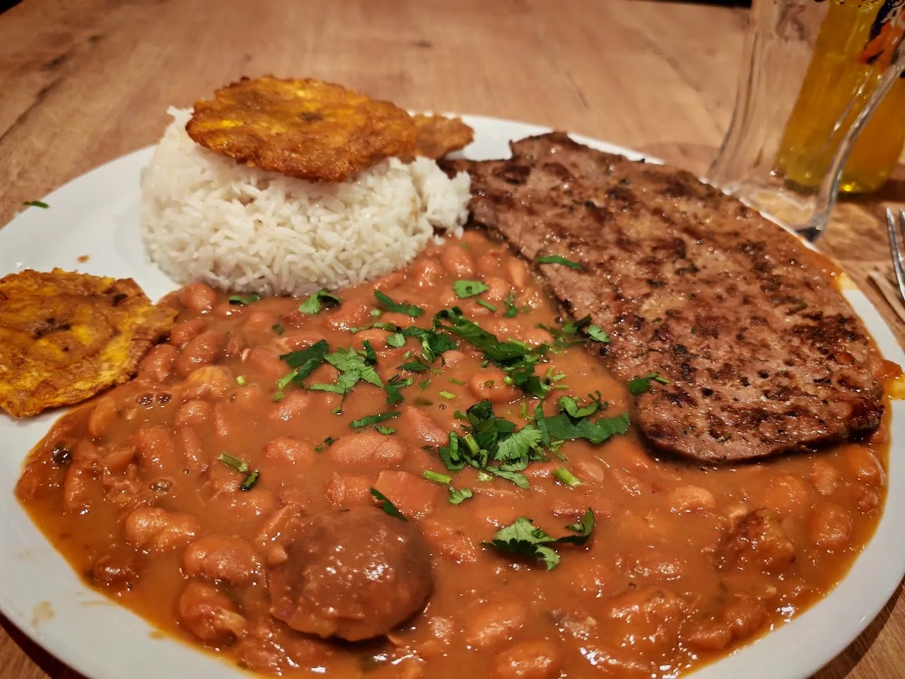 A plate of rice, stewed beans, grilled meat, and fried plantain