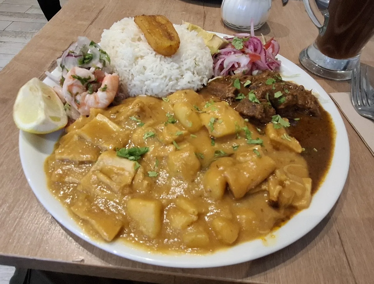 A plate of rice with a meat and vegetable curry, lime, and pickled onion