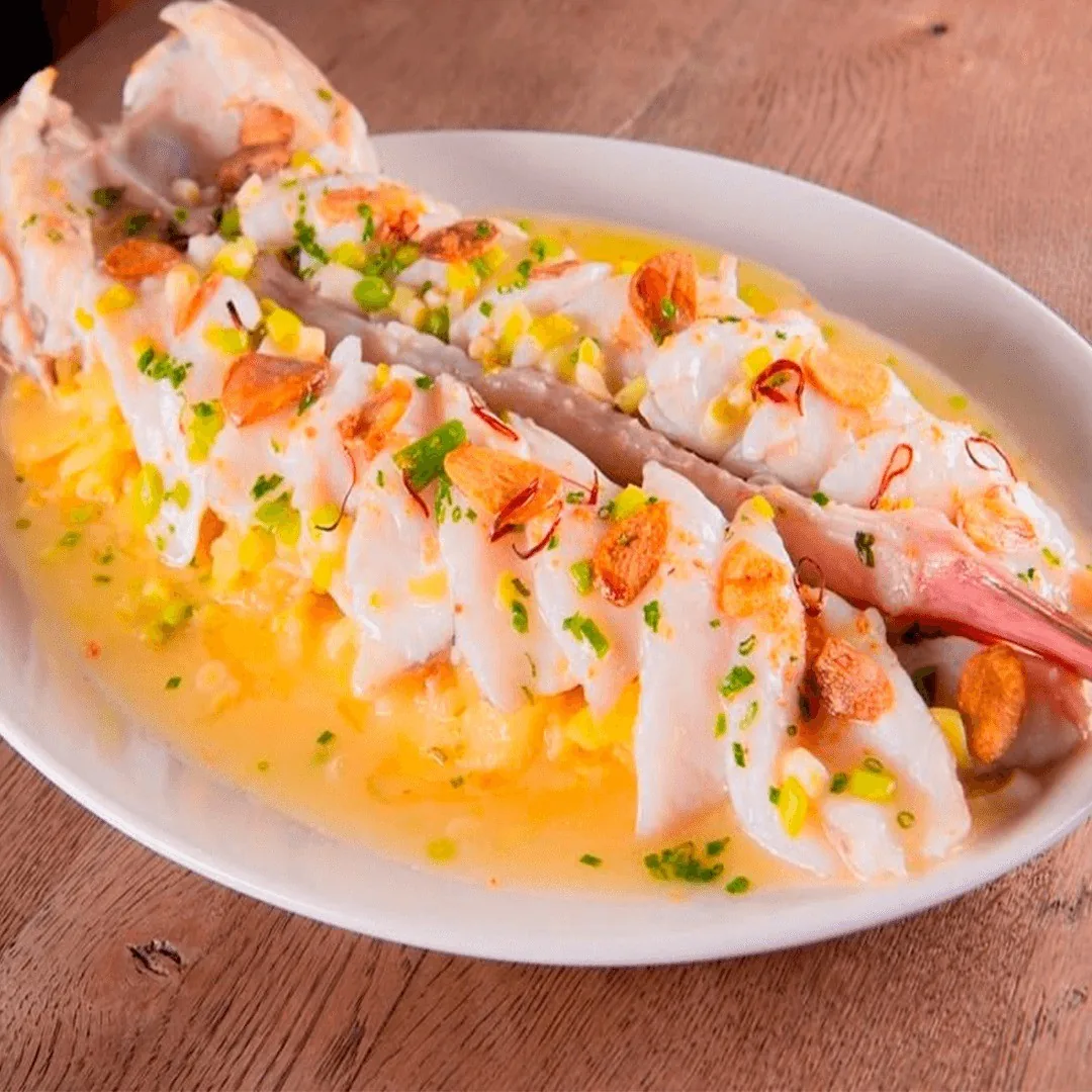 A plate of thinly sliced white fish with a bright yellow sauce and chopped garnish