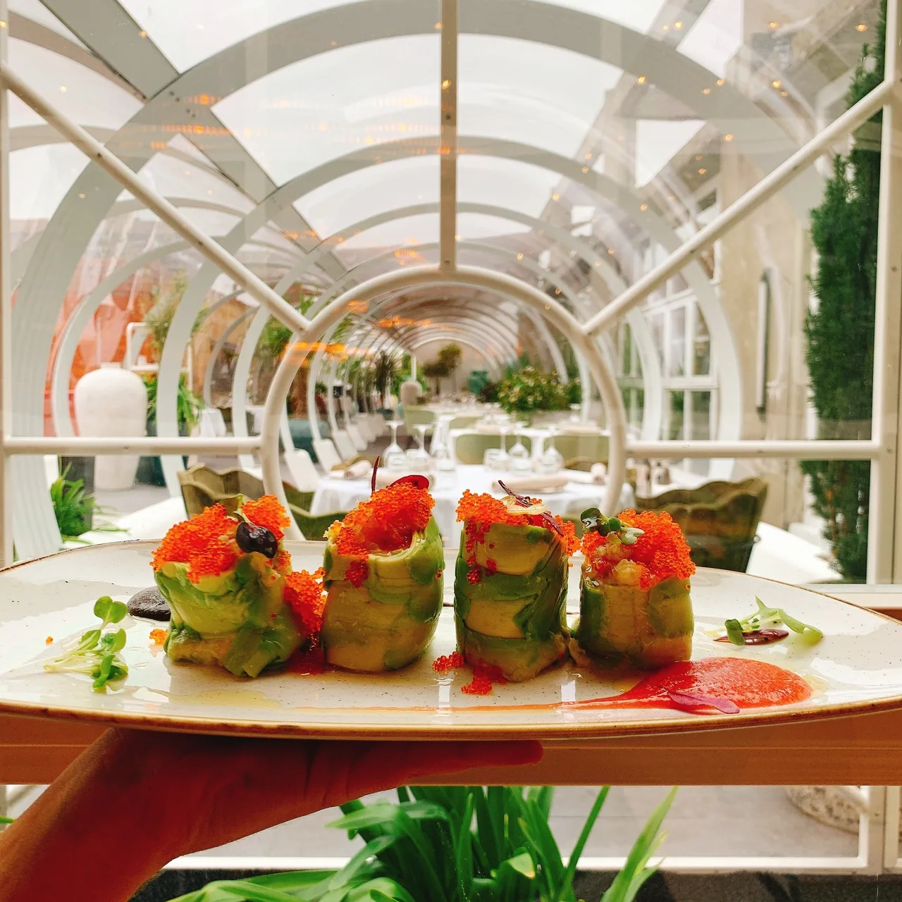 A plate of small vegetable-wrapped bites inside a glass-roofed garden dining space