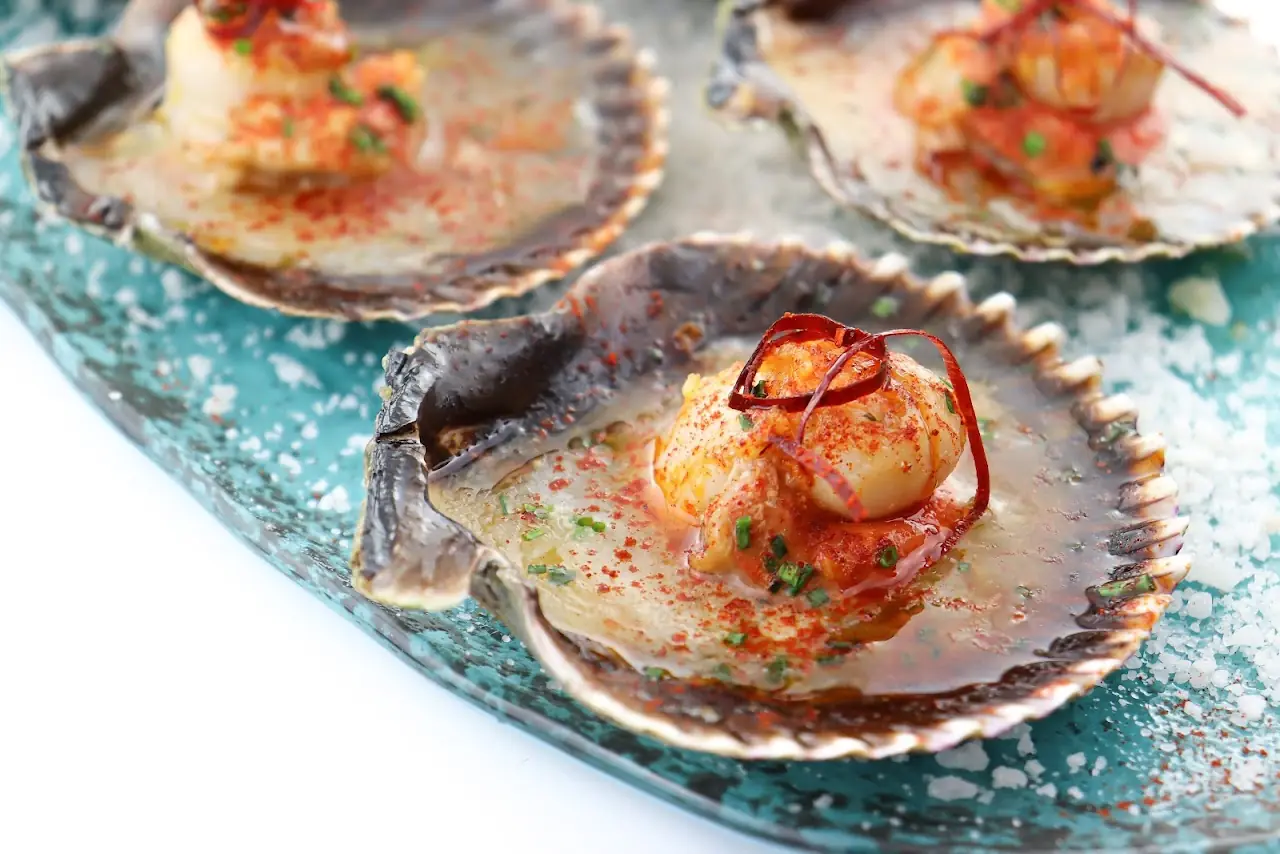 Scallops on the half shell topped with a red sauce and herbs.