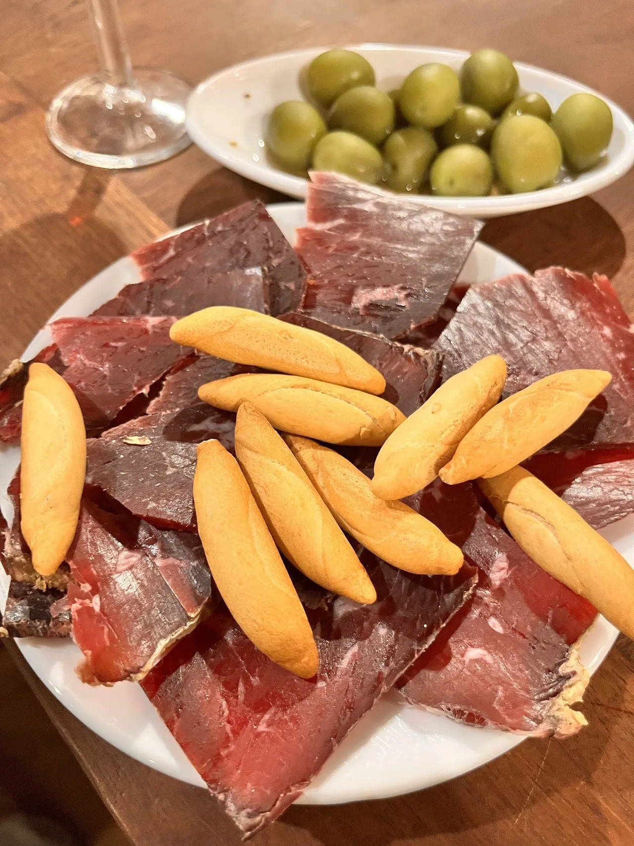 A plate of cured meat slices with breadsticks and a bowl of green olives